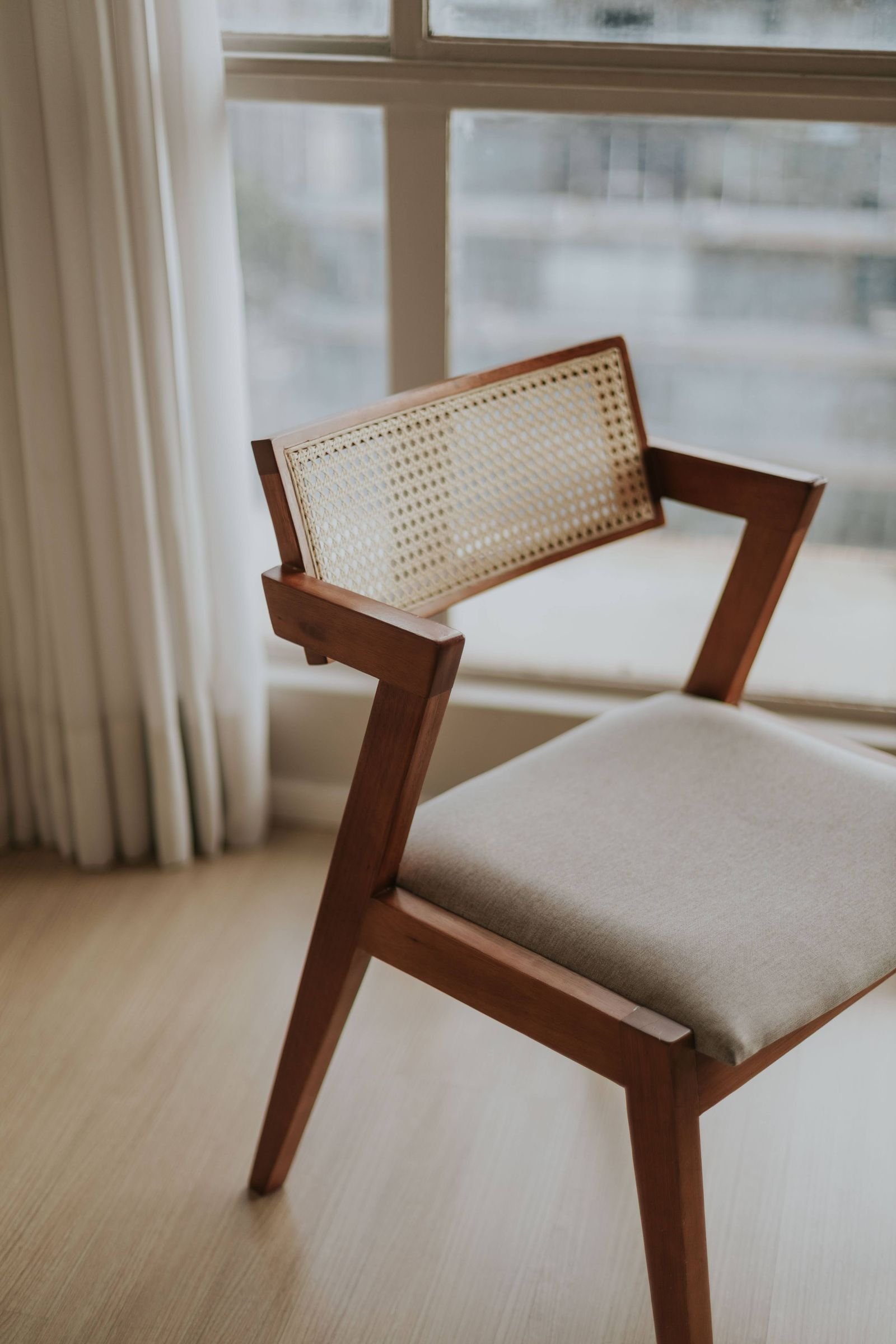 Mid-century wooden chair with a fabric seat in a bright sunlit room.