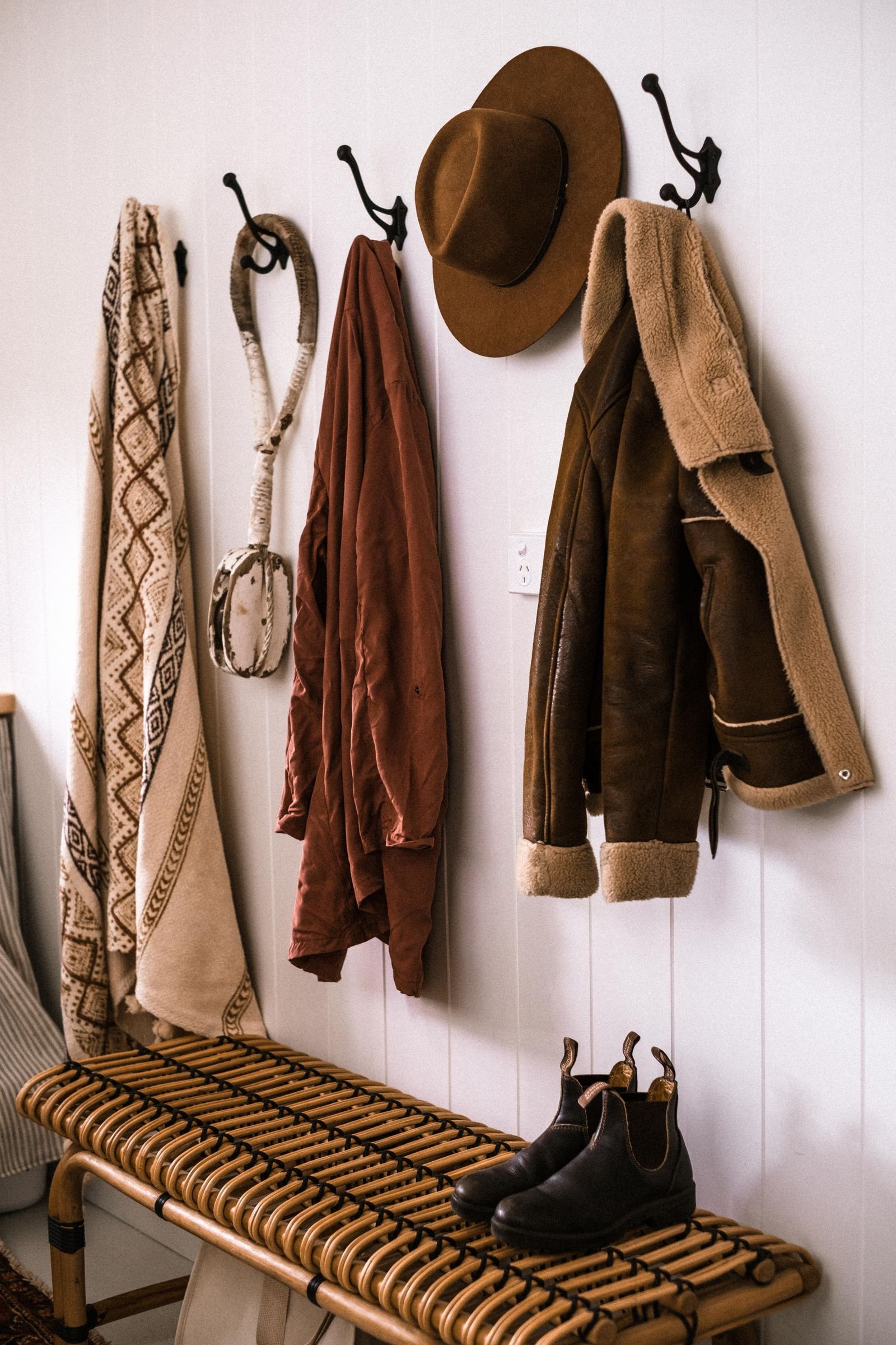 Rustic entryway with coats on wall hooks and boots under a bench
