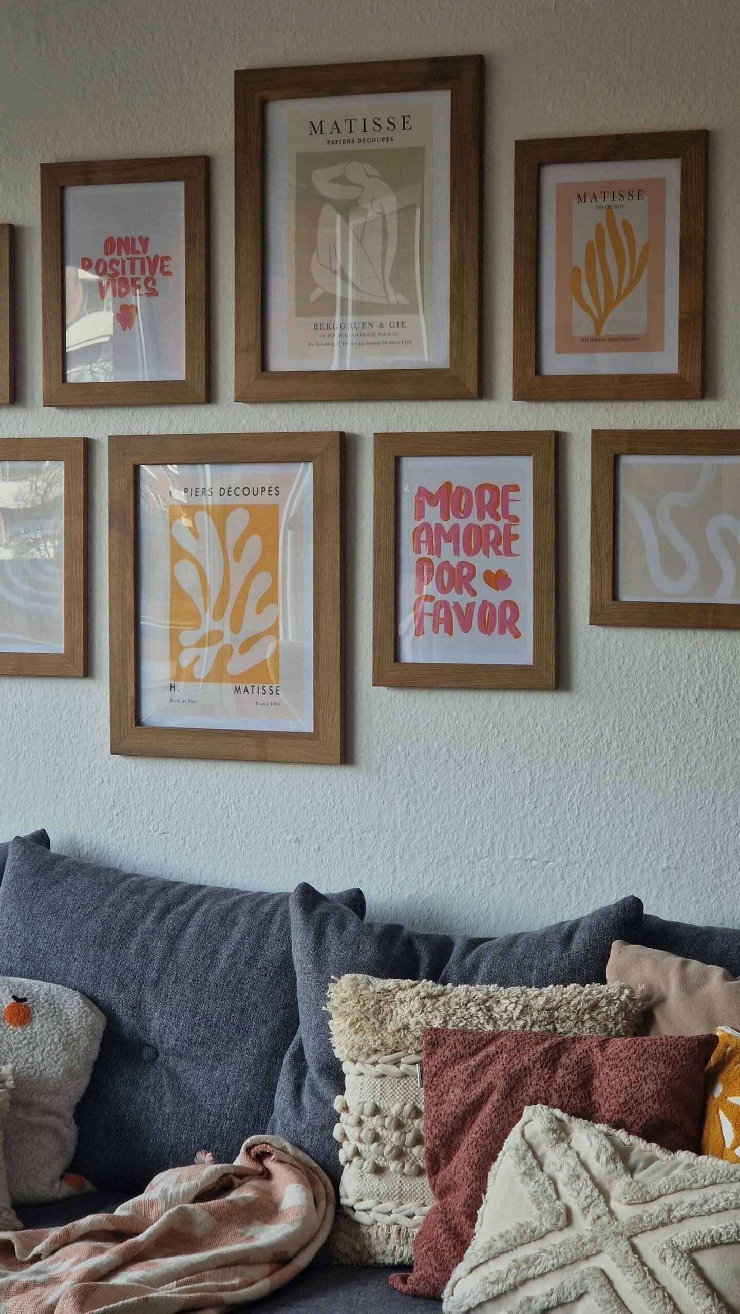 Simple framed art prints above a grey sofa with pillows in a calm living room