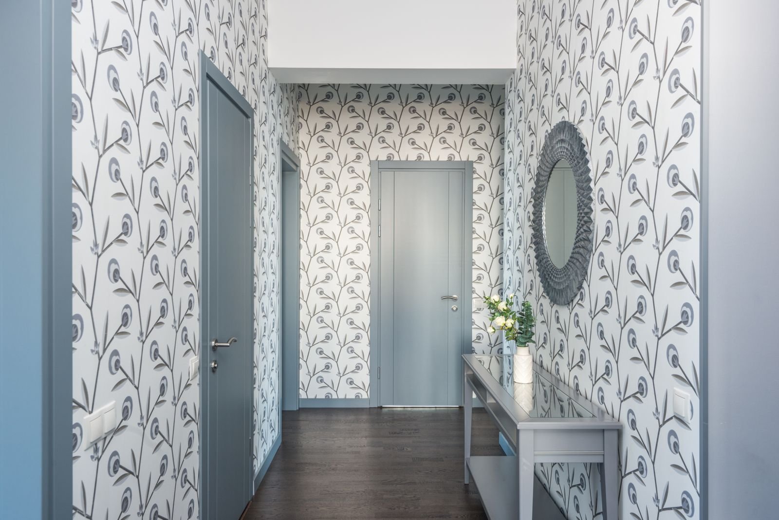 Floral wallpaper behind a console table and mirror in a hallway