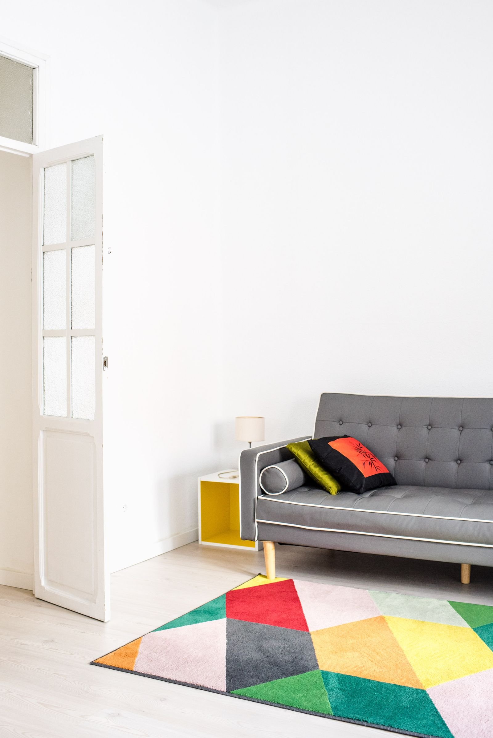 Grey sofa with a geometric rug and a white accent in a minimal living room
