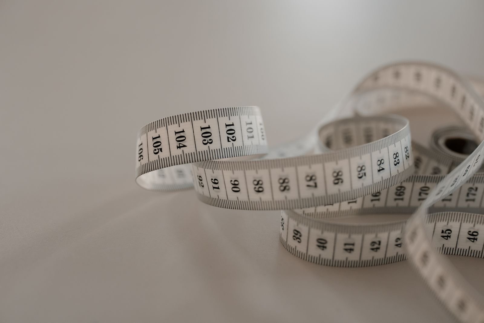 White tape measure with black numbers coiled on a plain surface