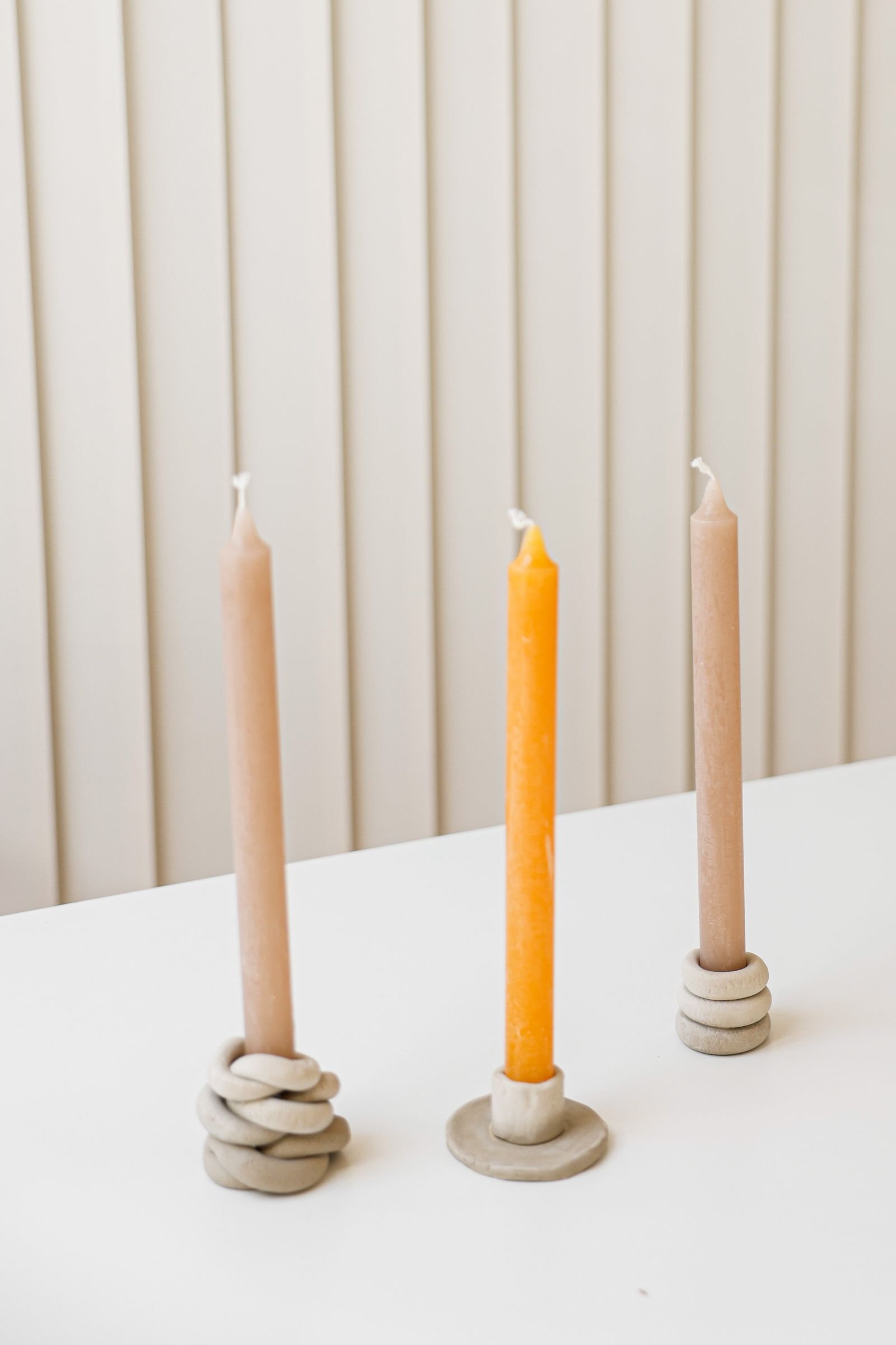 Three candles in handmade stone candlesticks arranged against a neutral wall