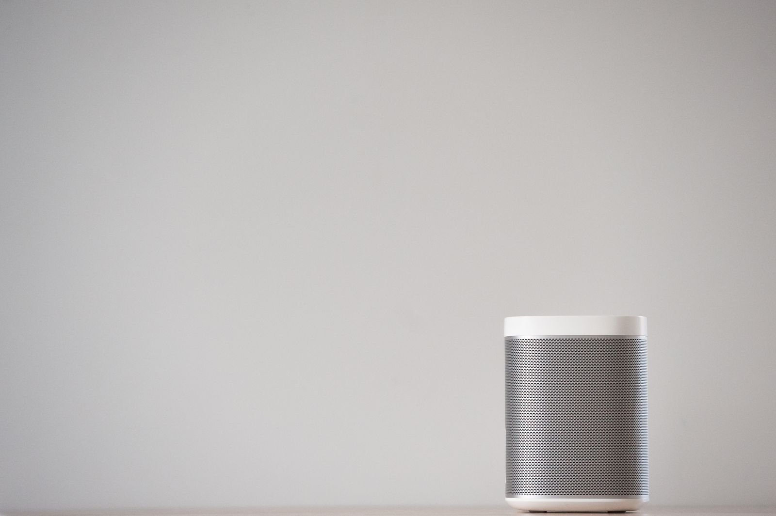 Sleek wireless speaker on a wooden table against a plain wall for ambient sound at home