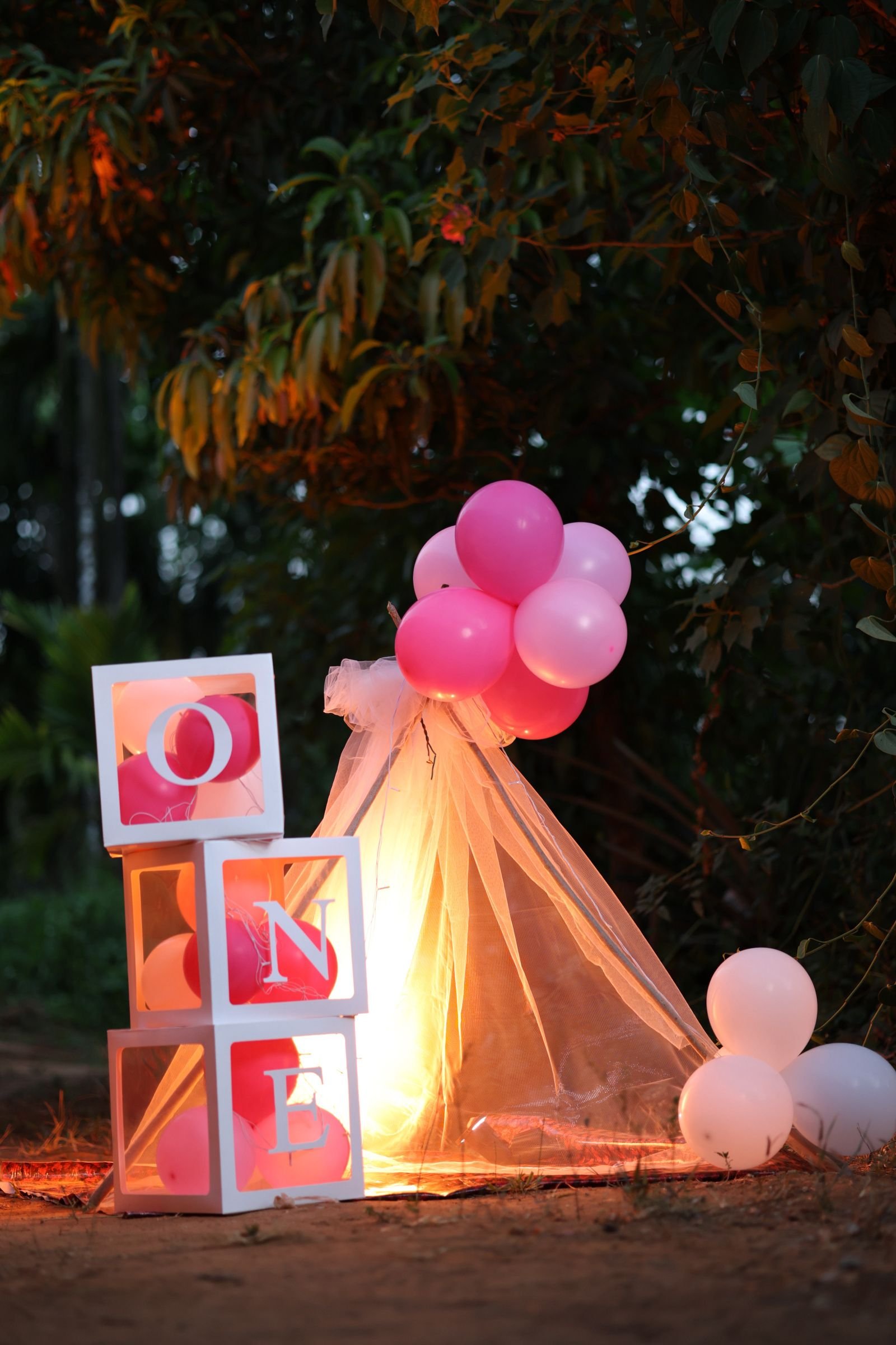 Pink balloons and letter blocks decorating an outdoor birthday setup
