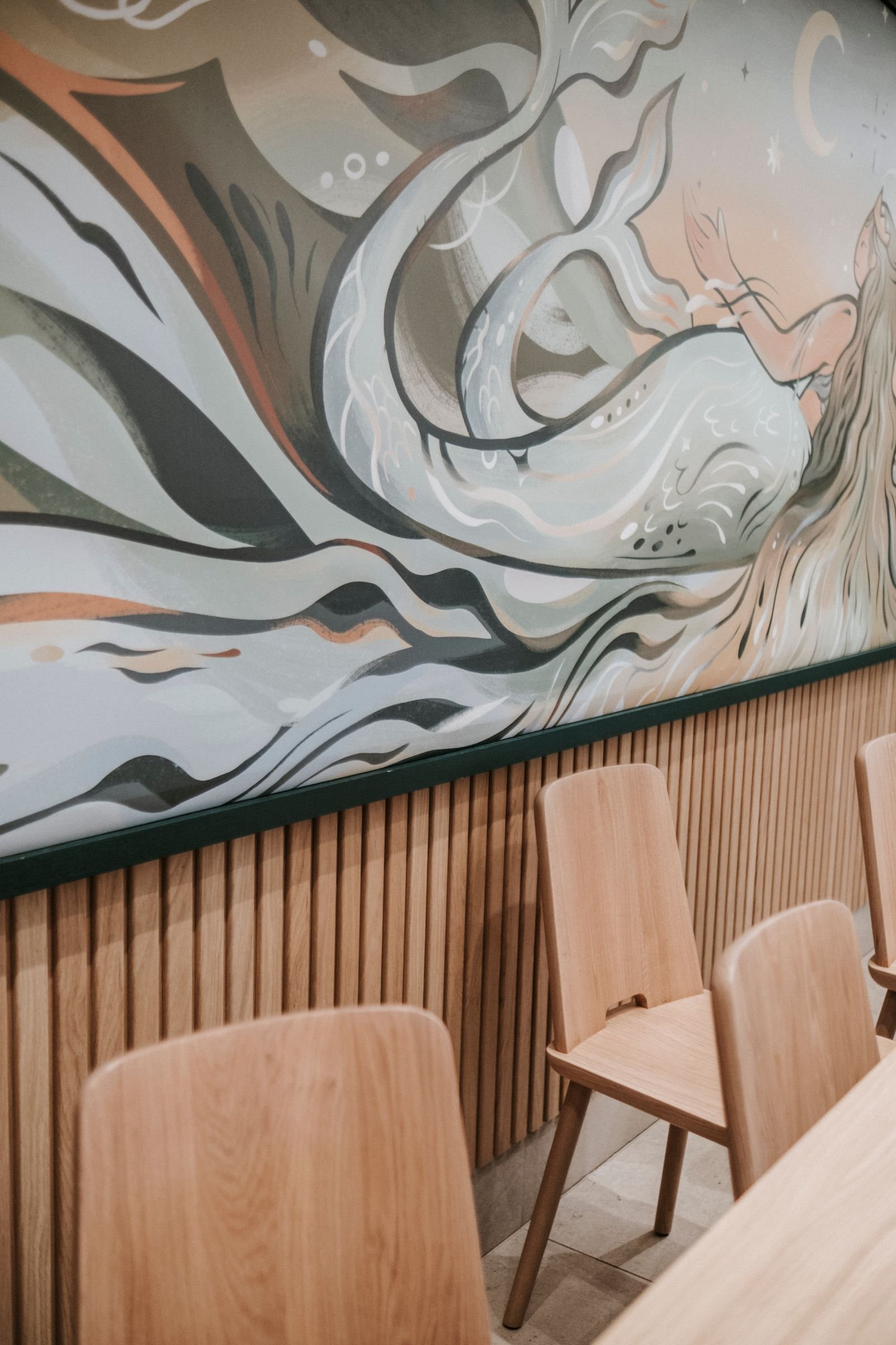 Abstract earth-toned mural painted on the wall behind a wooden dining table and chairs
