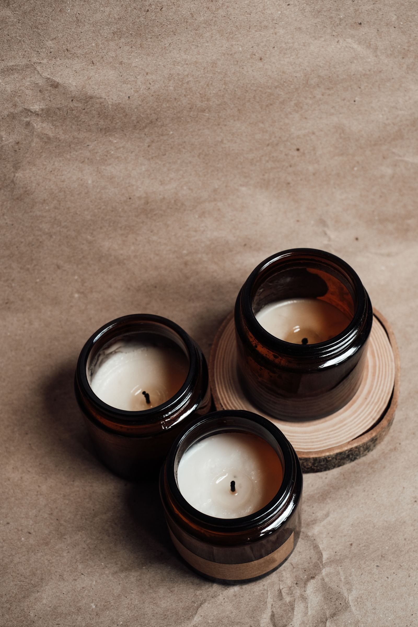 Three scented candles in amber glass jars on a wooden slice