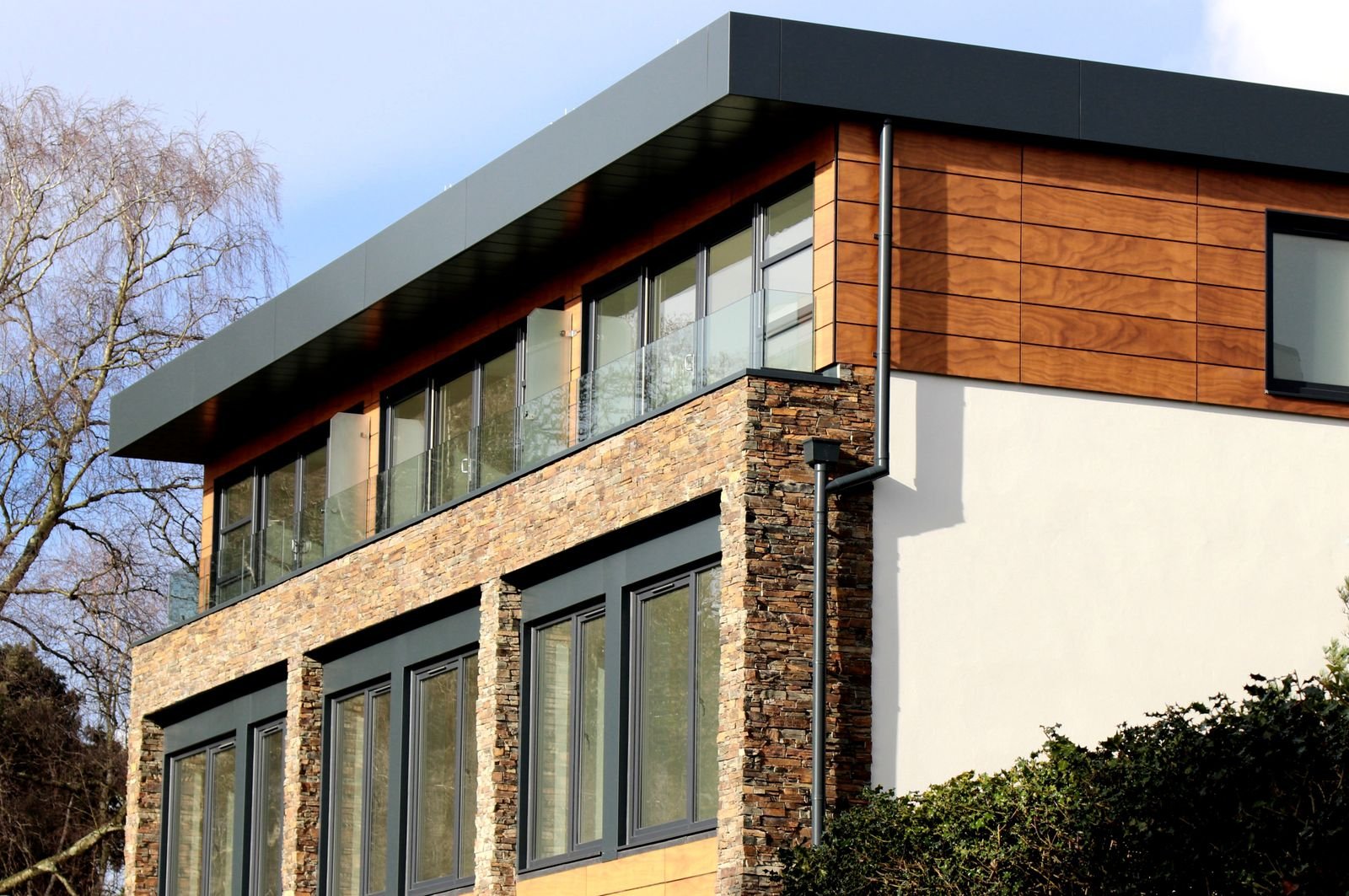 Modern stone and wood house with large windows seen against a clear sky