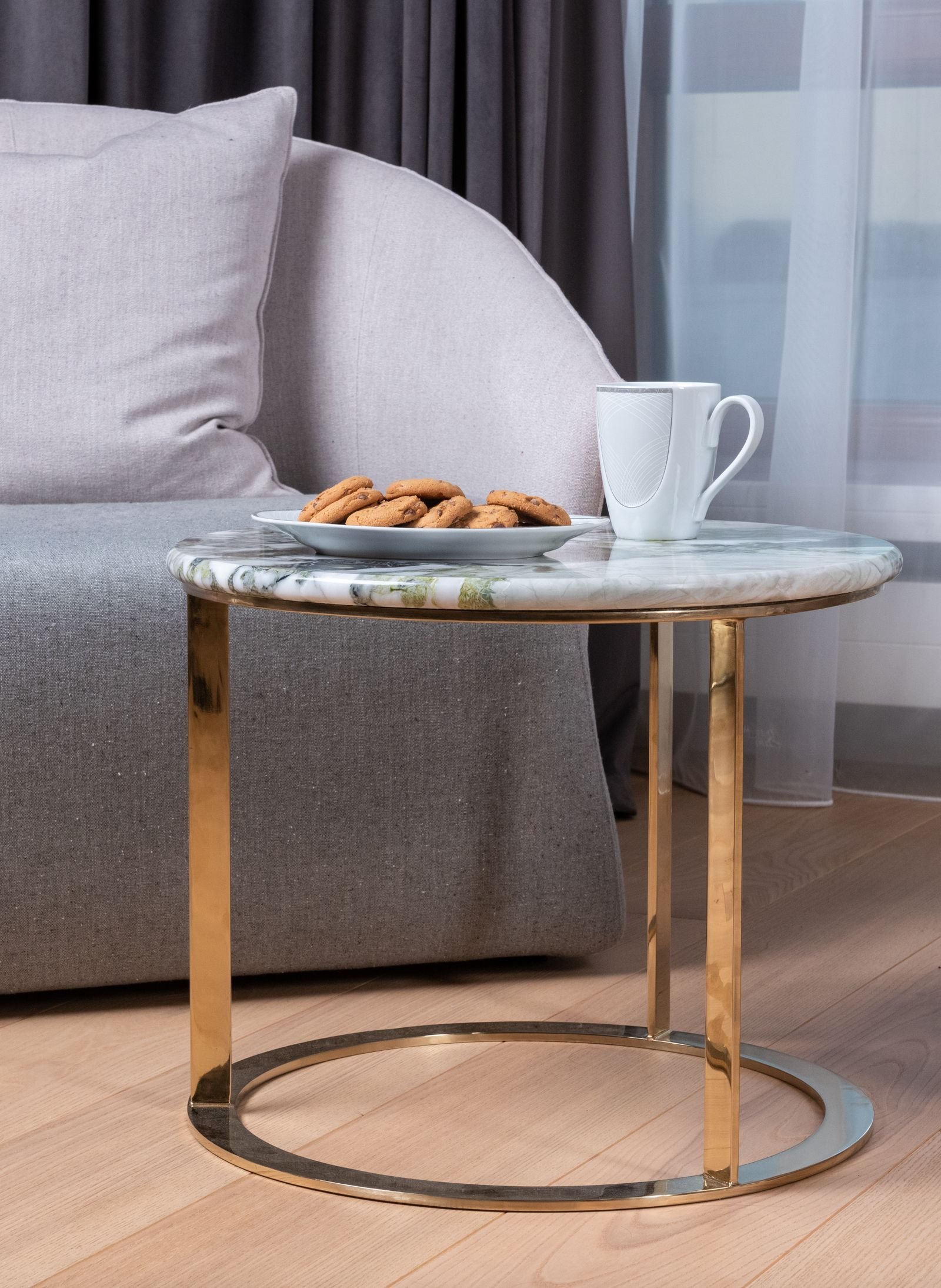 Round marble coffee table with golden metal legs beside a sofa