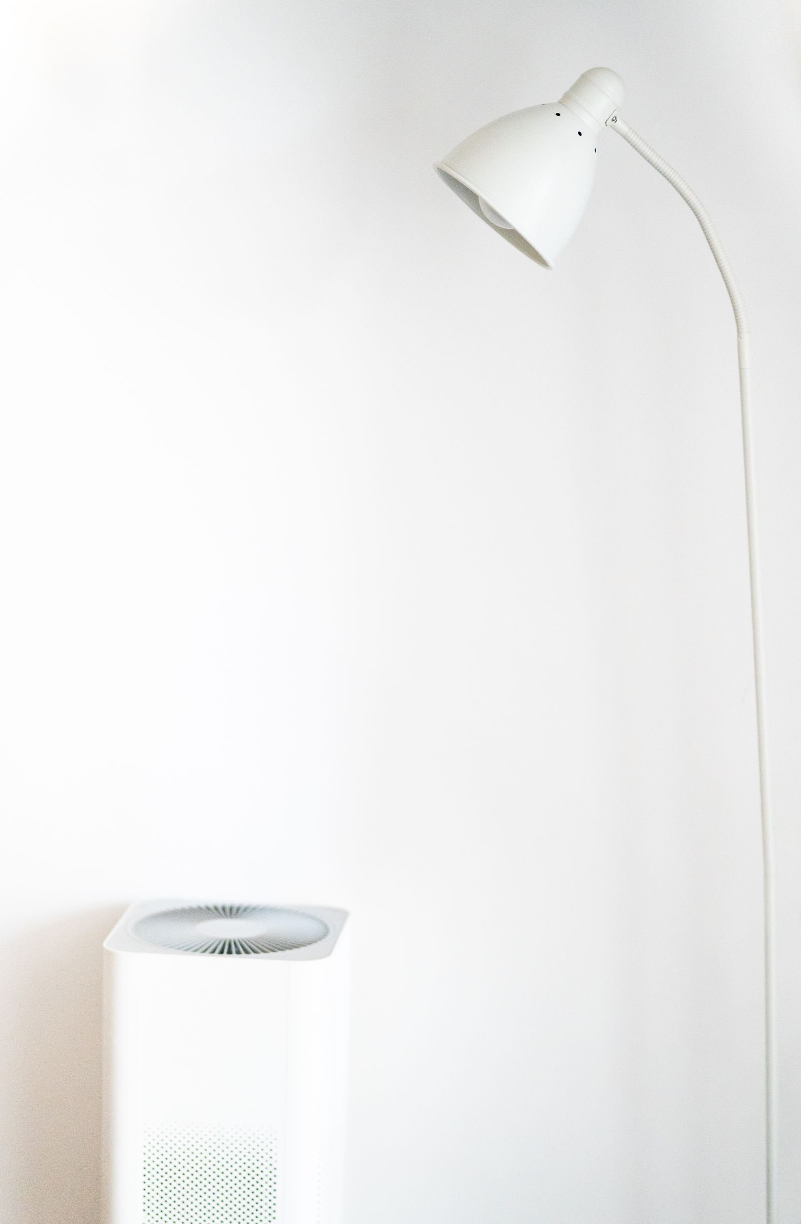 Air purifier standing beside a white floor lamp against a plain wall.