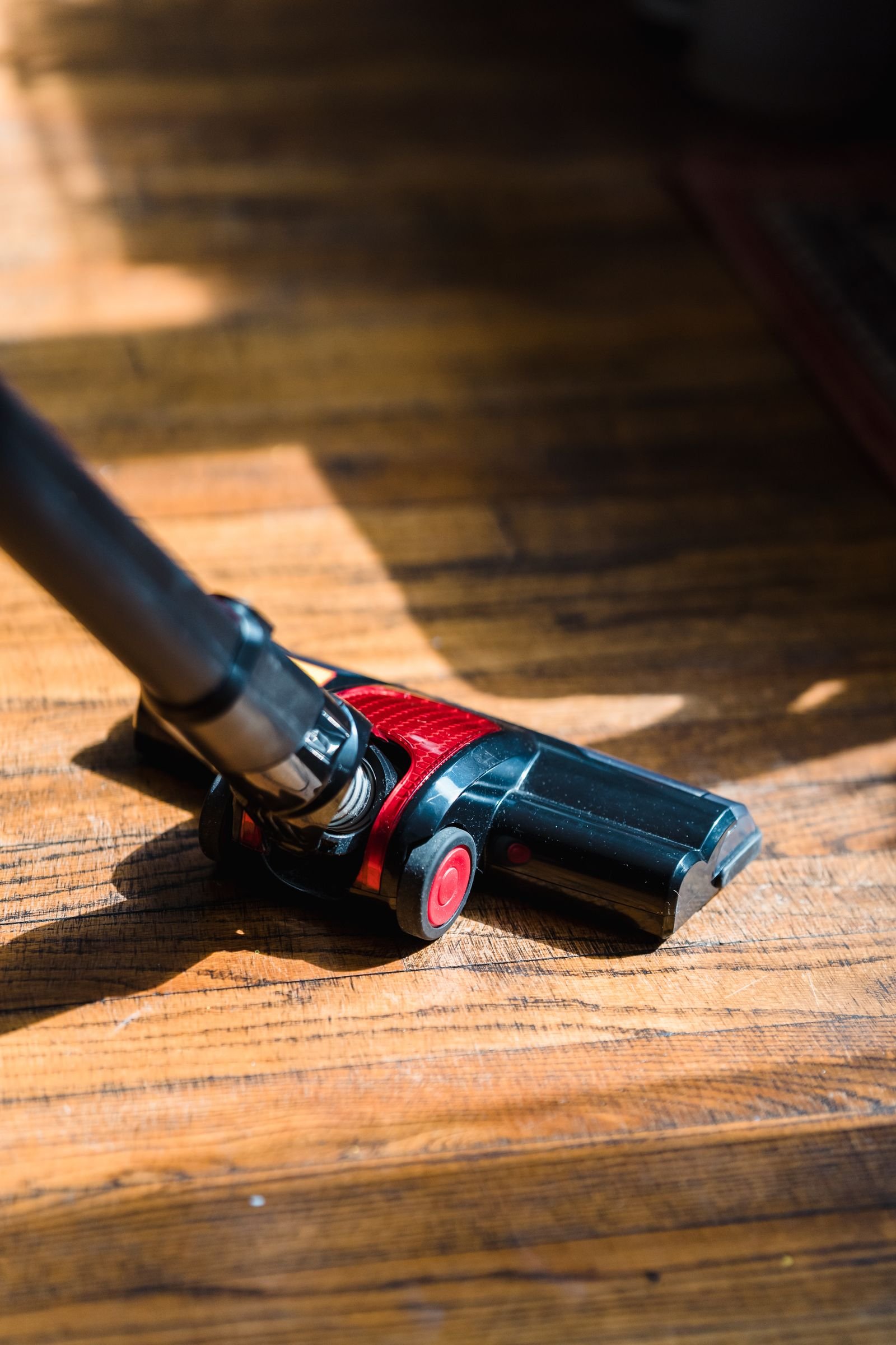 Vacuum cleaner head working across a sunlit wooden floor.