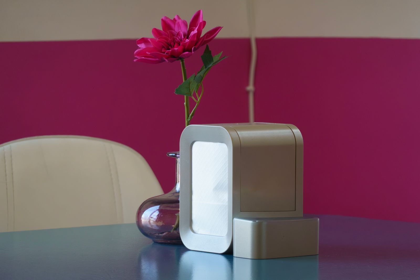 Sleek air purifier next to a vase with a pink flower on a table.
