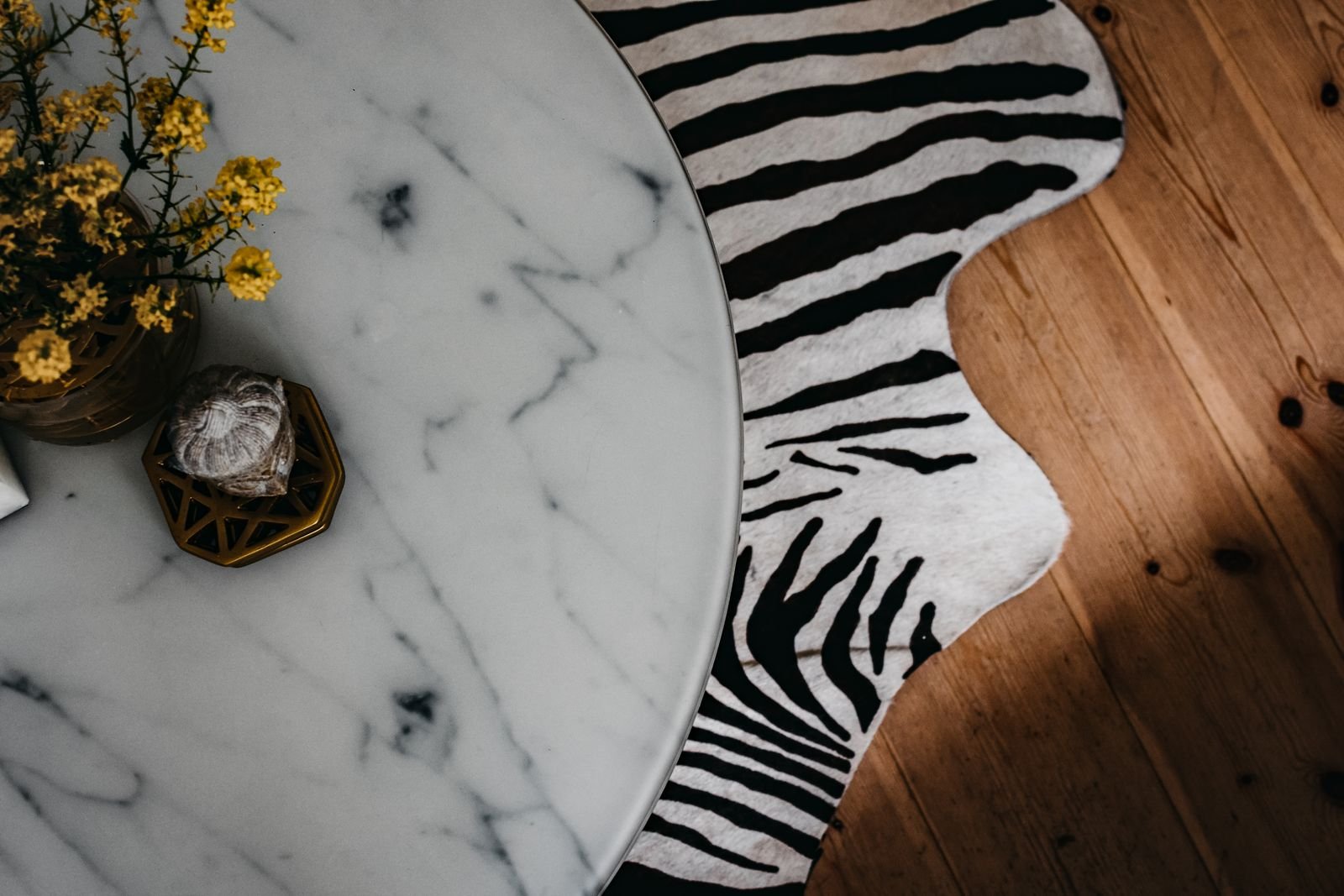 Yellow flowers and a figurine on a marble table above an animal-skin rug.