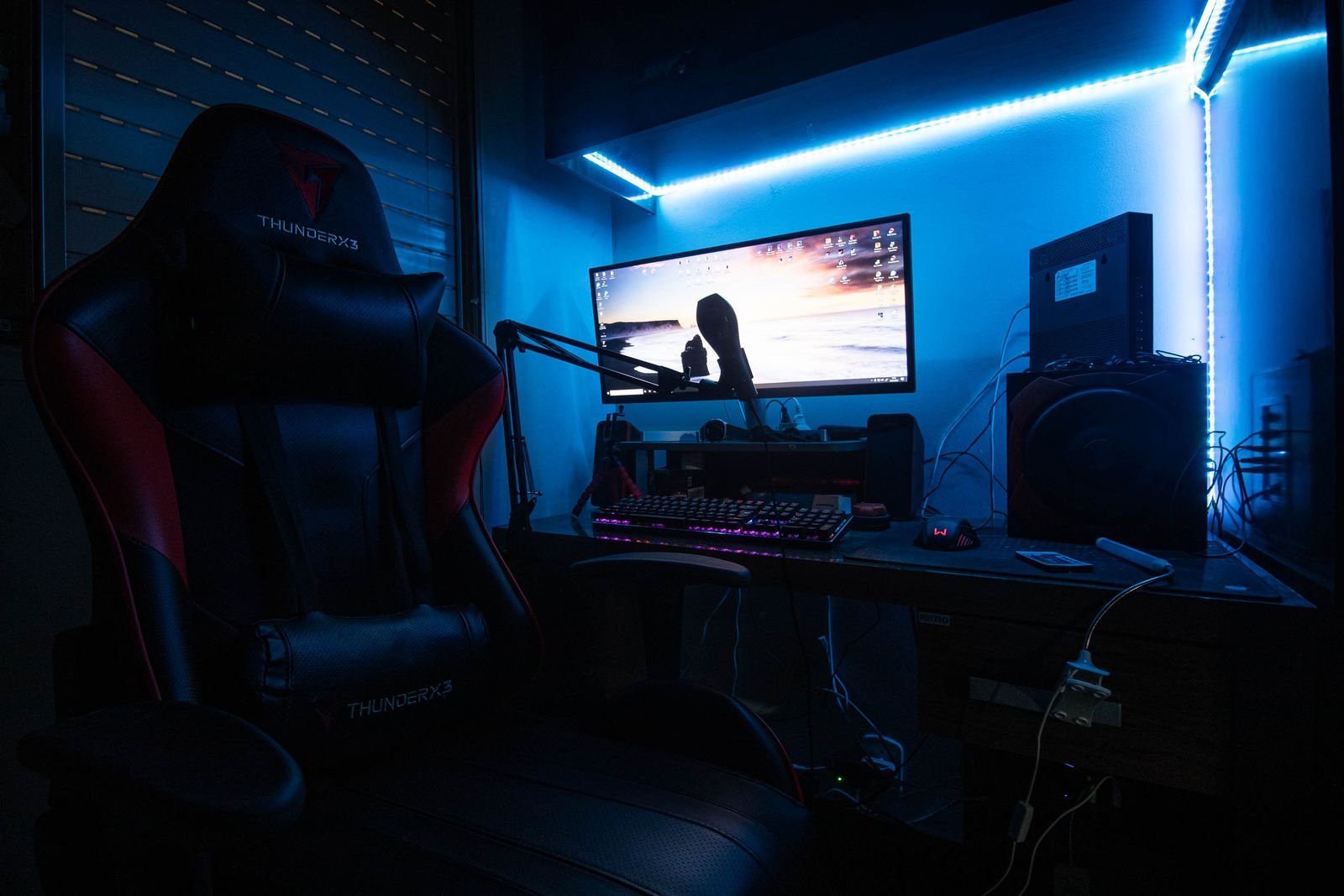 Desk with a monitor, speakers and a gaming chair lit by blue LED light.