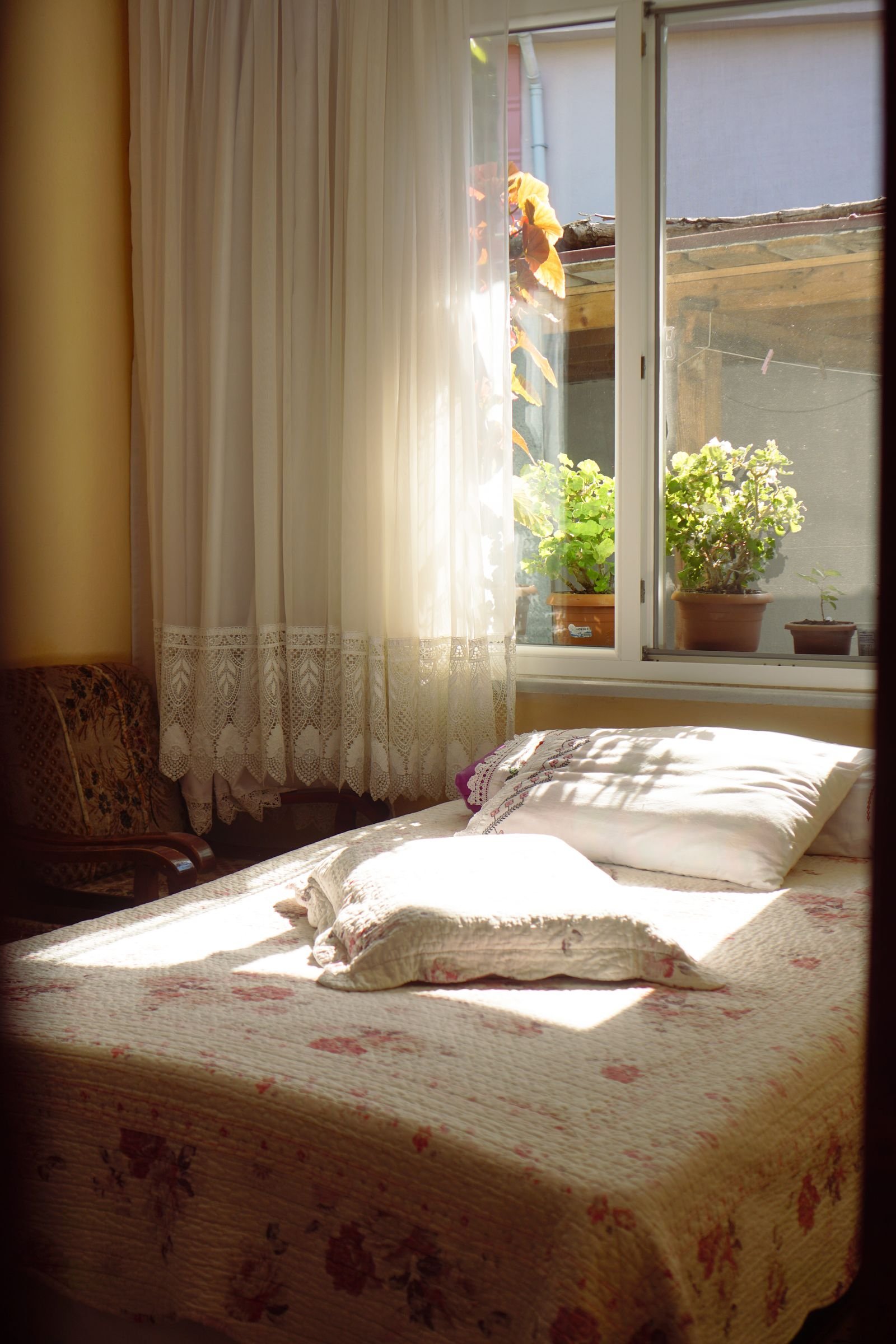 Sunlit bedroom with lace curtains and a floral bedspread.