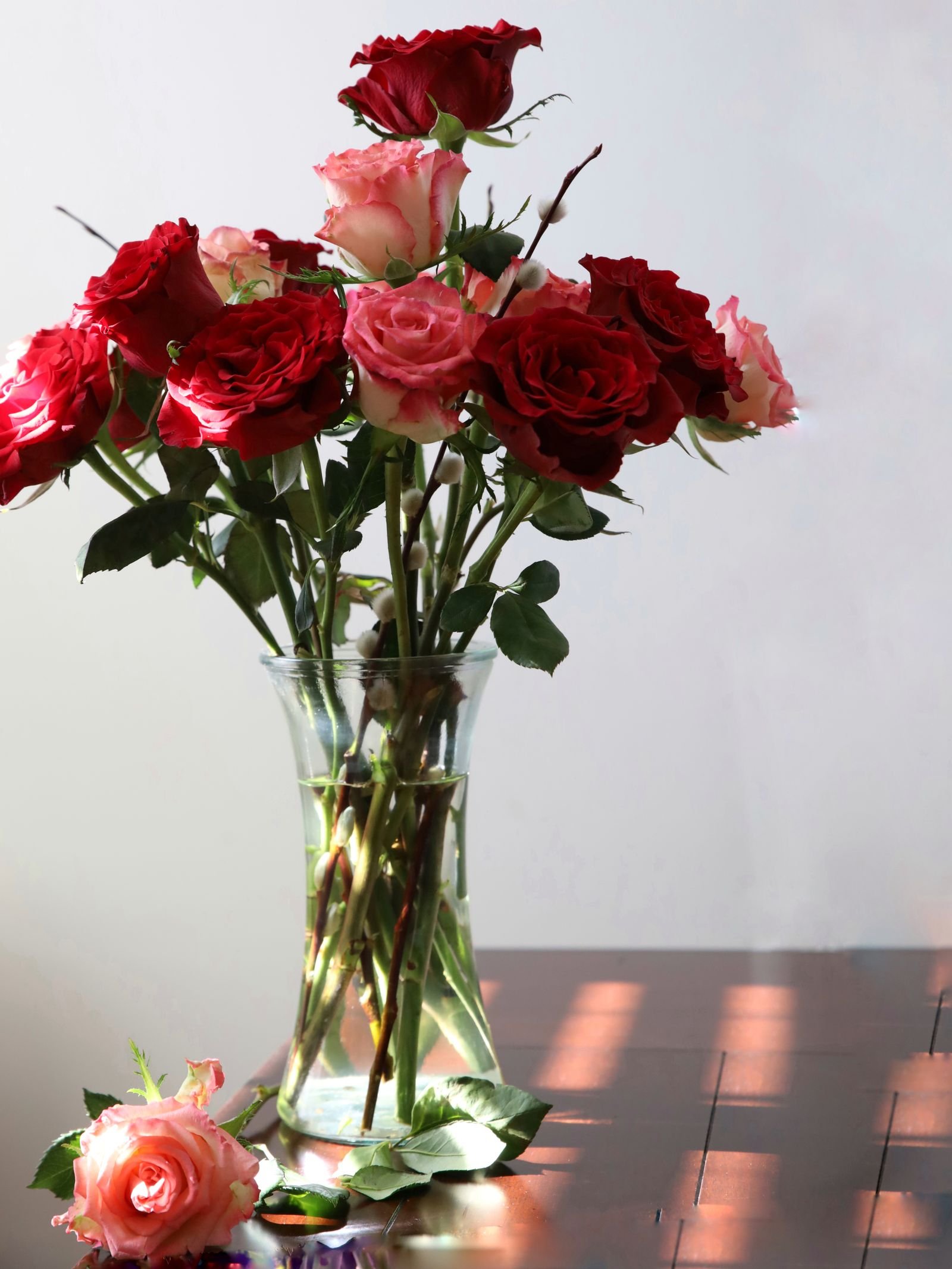 Fresh red and pink roses in a clear glass vase.