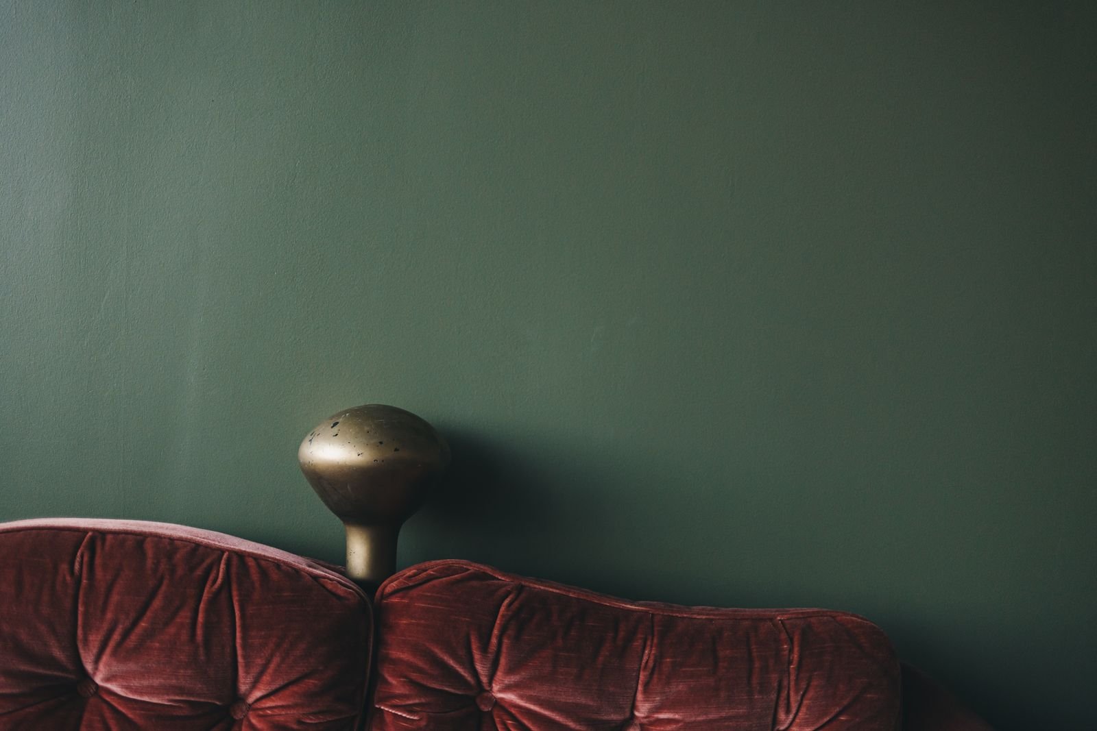 Velvet sofa against a deep green wall beside a vintage lamp.