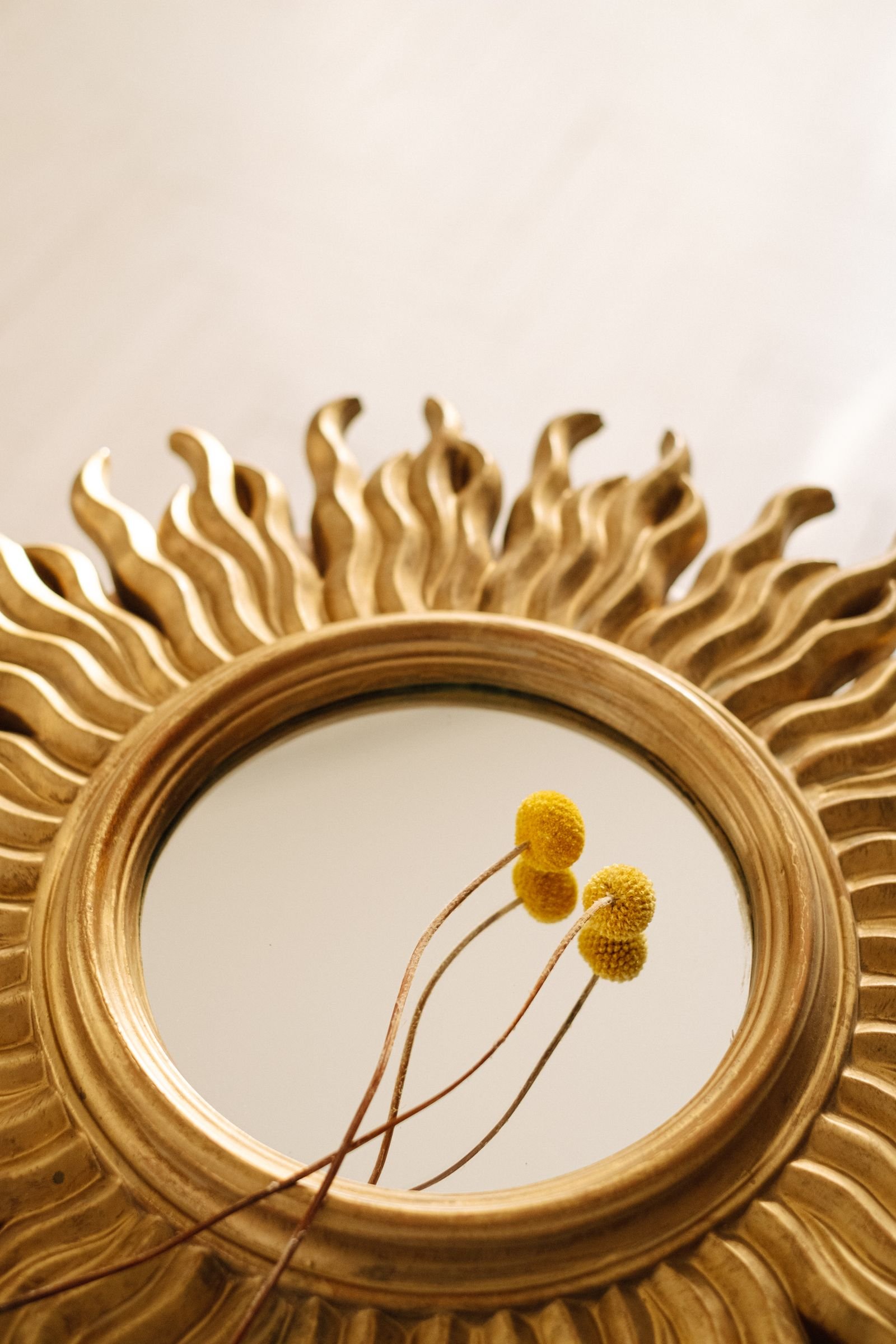 Sunburst mirror reflecting dried yellow flowers.
