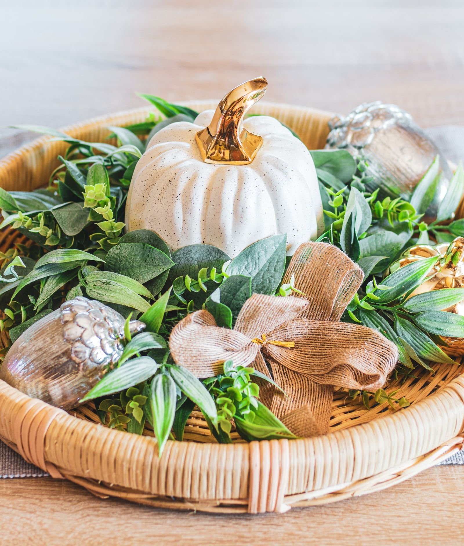 Decorative pumpkin with greenery and metallic accents on an autumn tray.