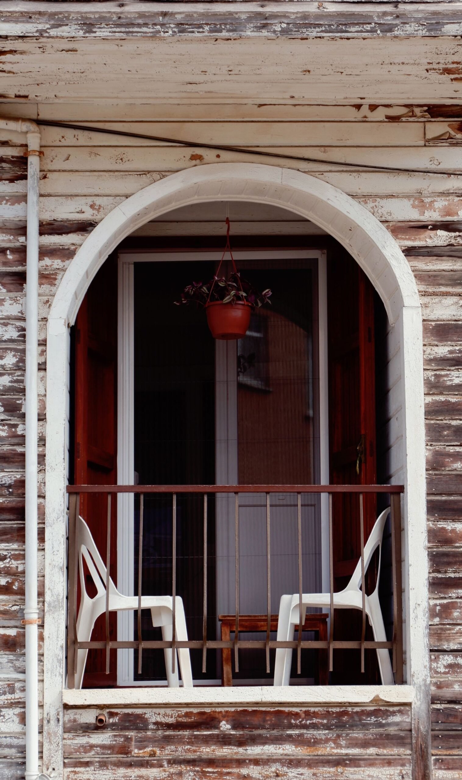 Wooden balcony with chairs and a hanging plant.