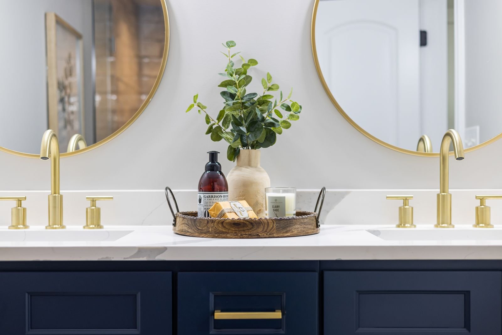 Bathroom vanity with gold faucets, round mirrors and chic accessories.
