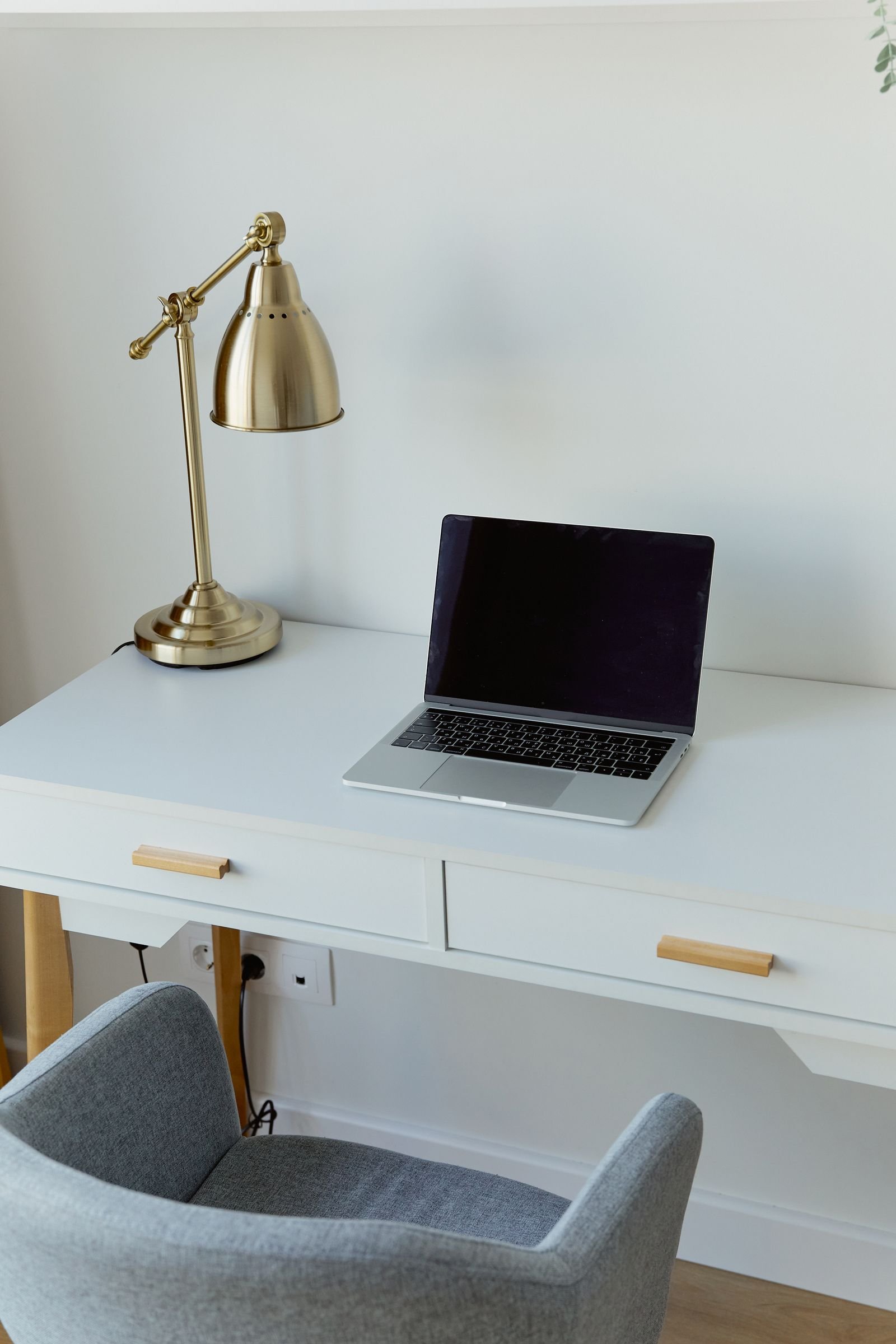 Home office desk with a laptop, a gold lamp and an elegant chair.