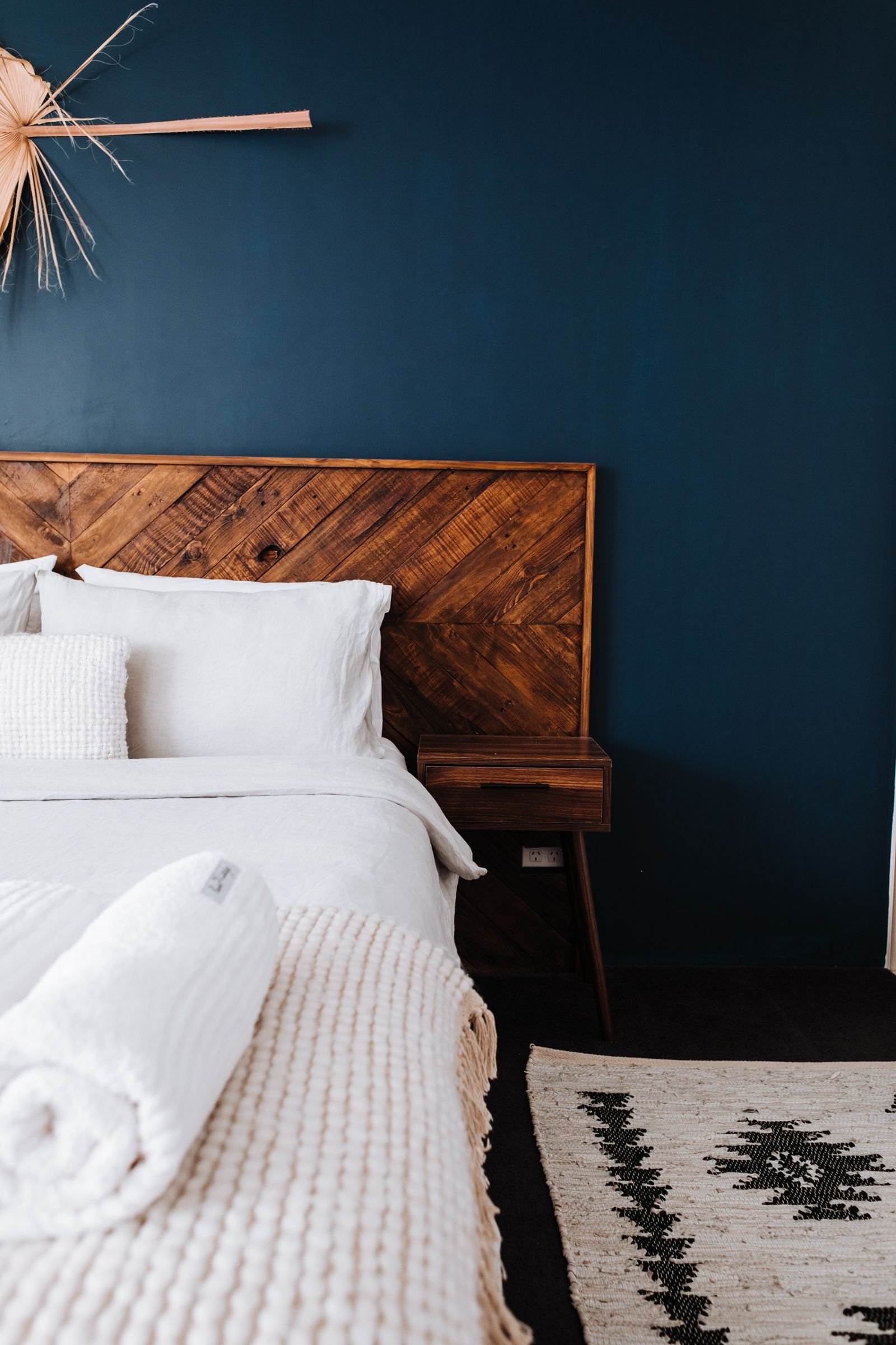 Minimalist bedroom with a dark blue wall and a wooden headboard.