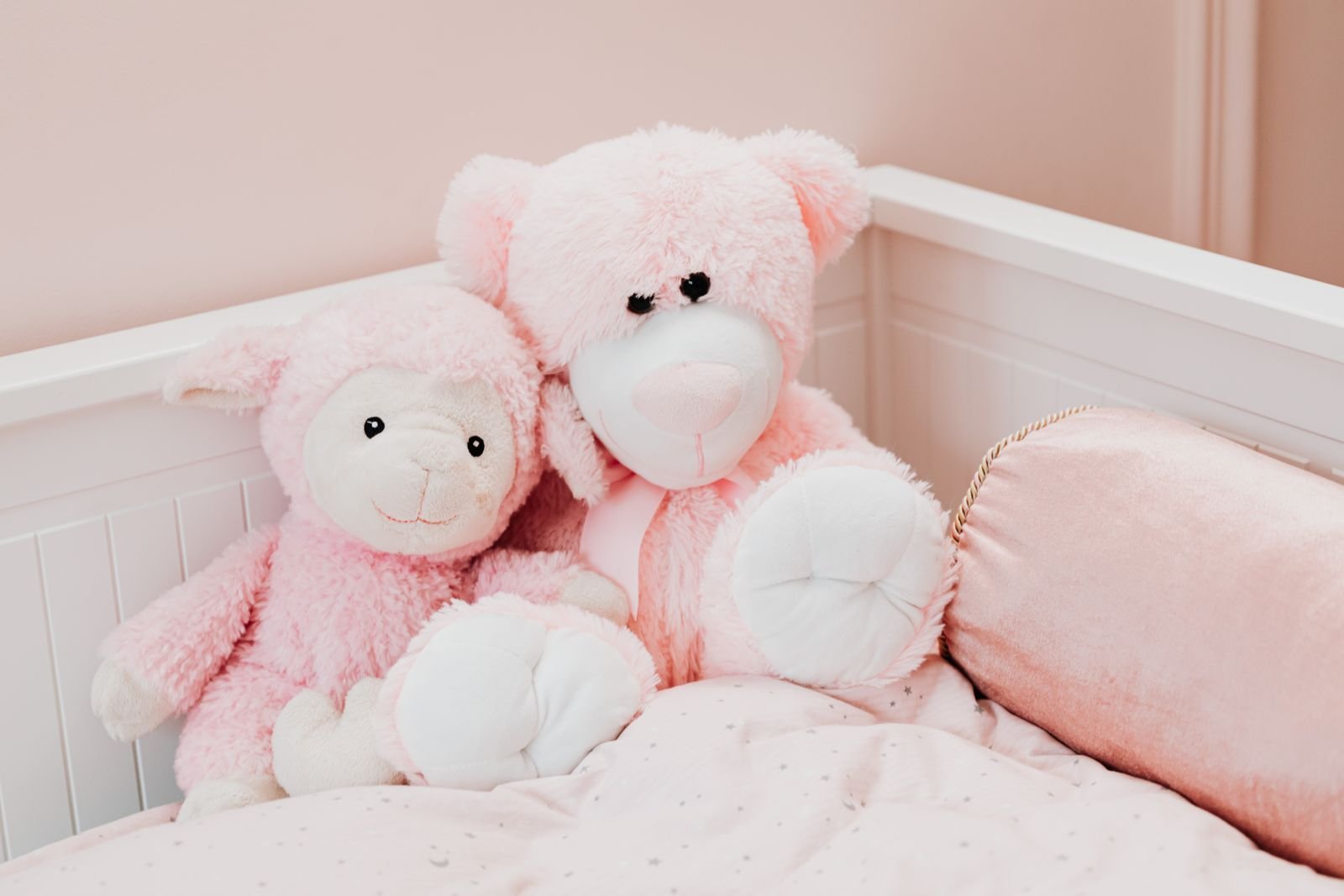 Pink plush toys on a white bed in a children's room.