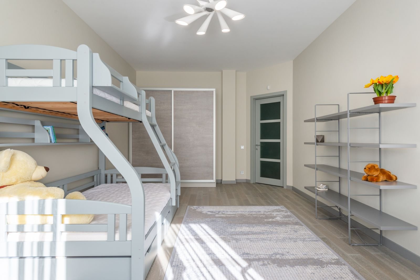 Bright bedroom with a bunk bed, a bear toy and shelves of flowerpots.