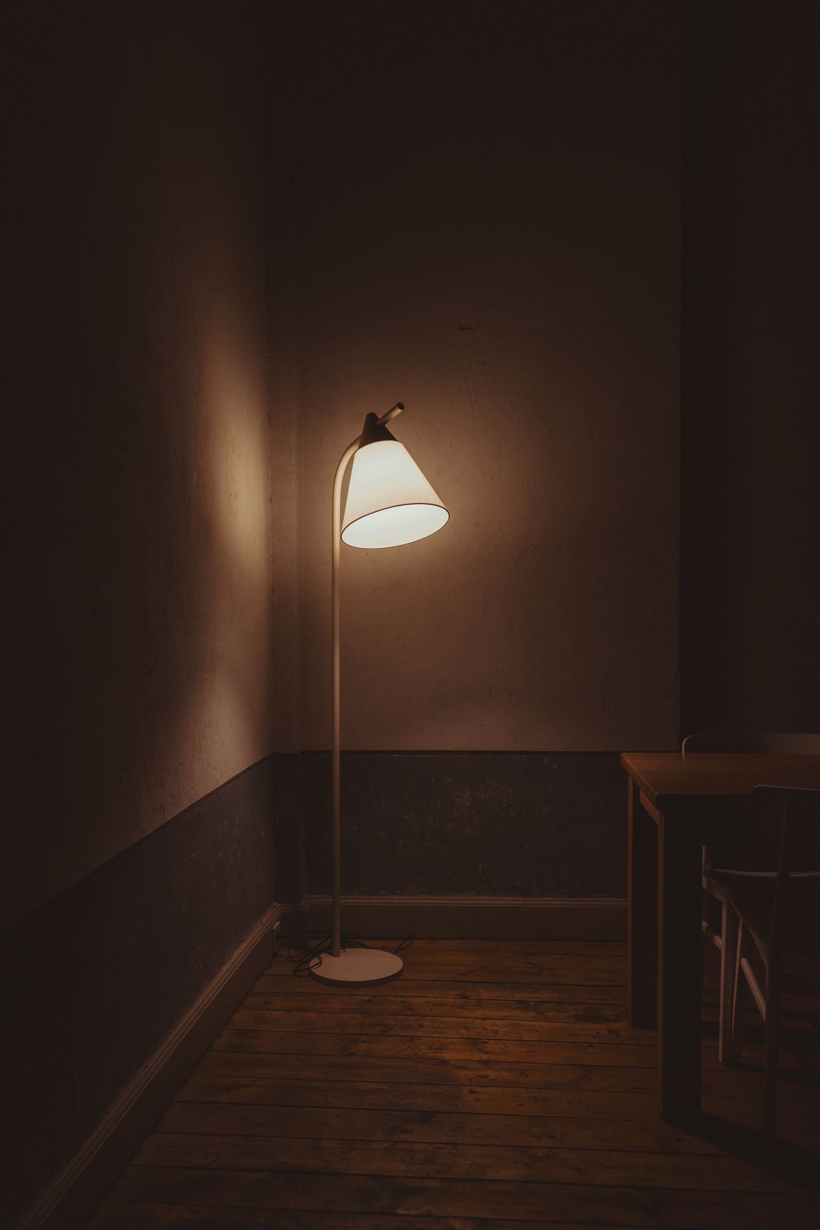 Minimalist room with a glowing floor lamp beside a wooden table.