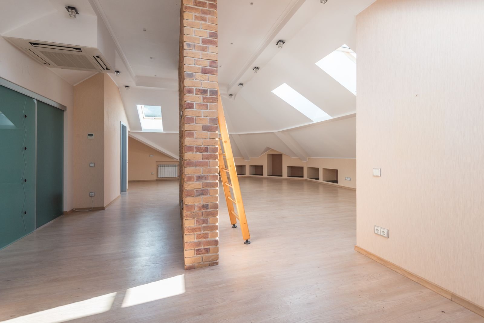 Spacious attic room lit by skylights, with a brick pillar and a wooden ladder.