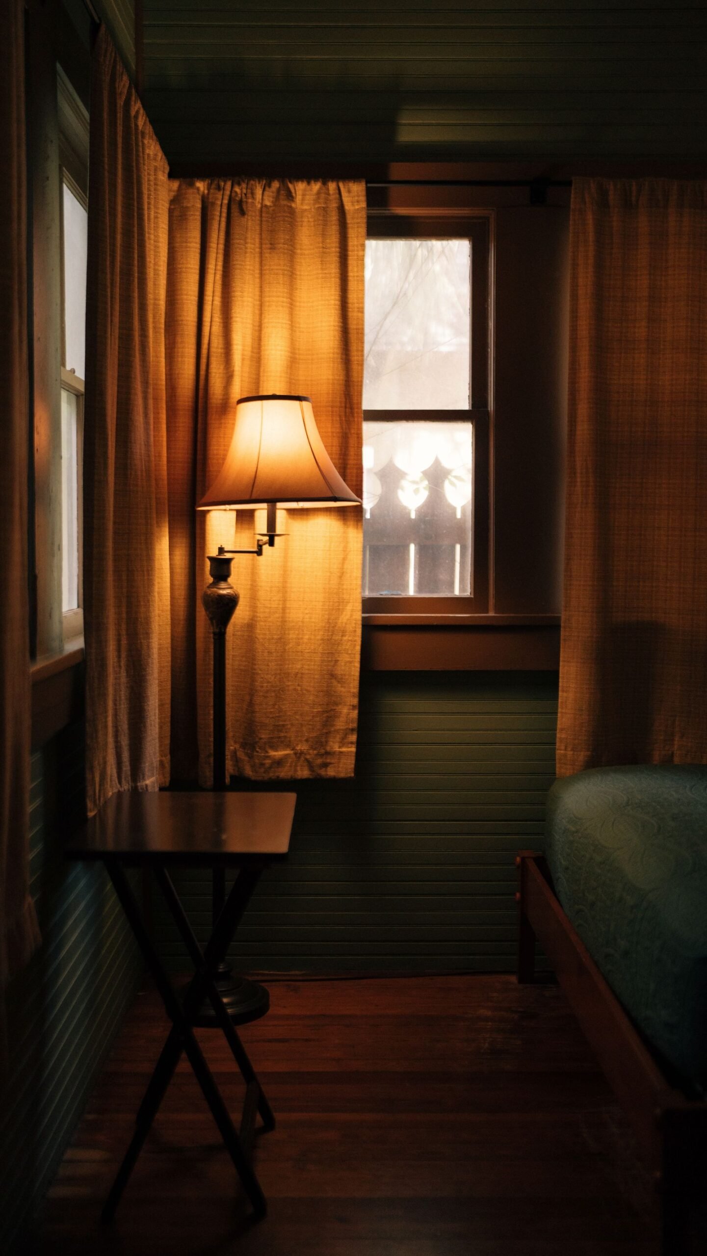 Cozy bedroom with a glowing floor lamp, curtains and wooden decor.