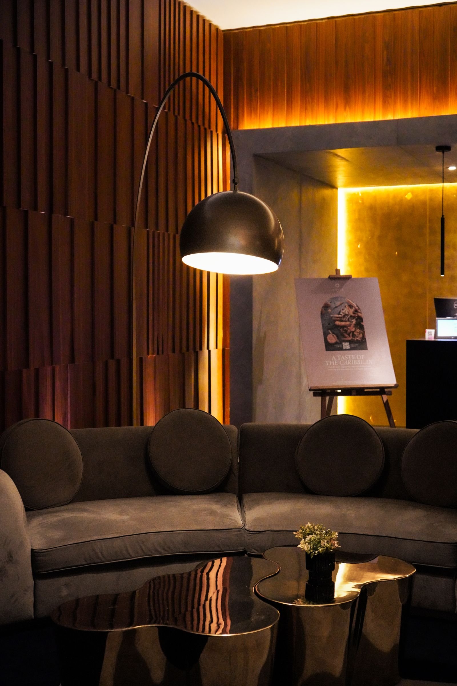 Warmly lit lounge with a curved sofa and a standing lamp.