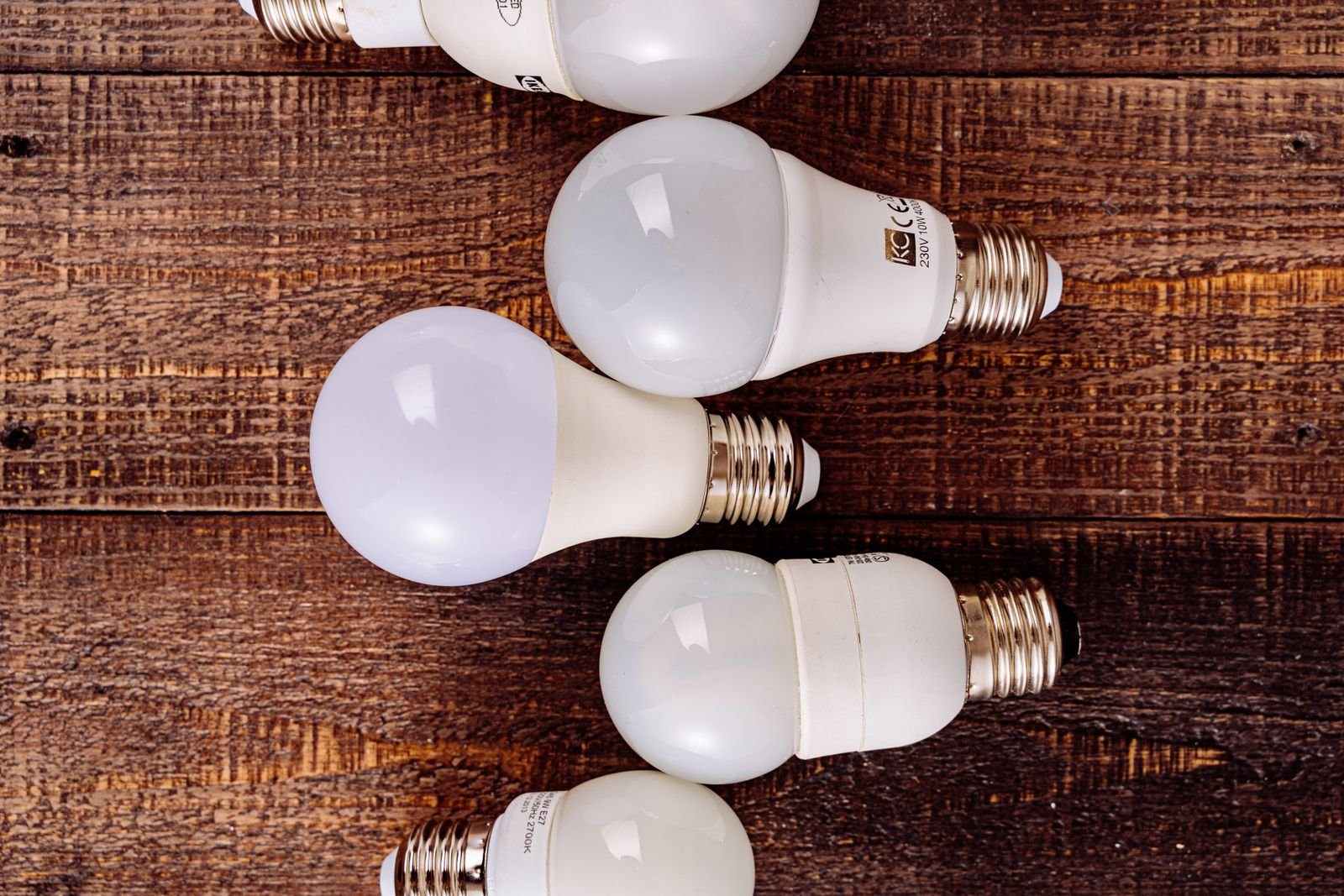 Several LED light bulbs lined up on a rustic wooden surface.