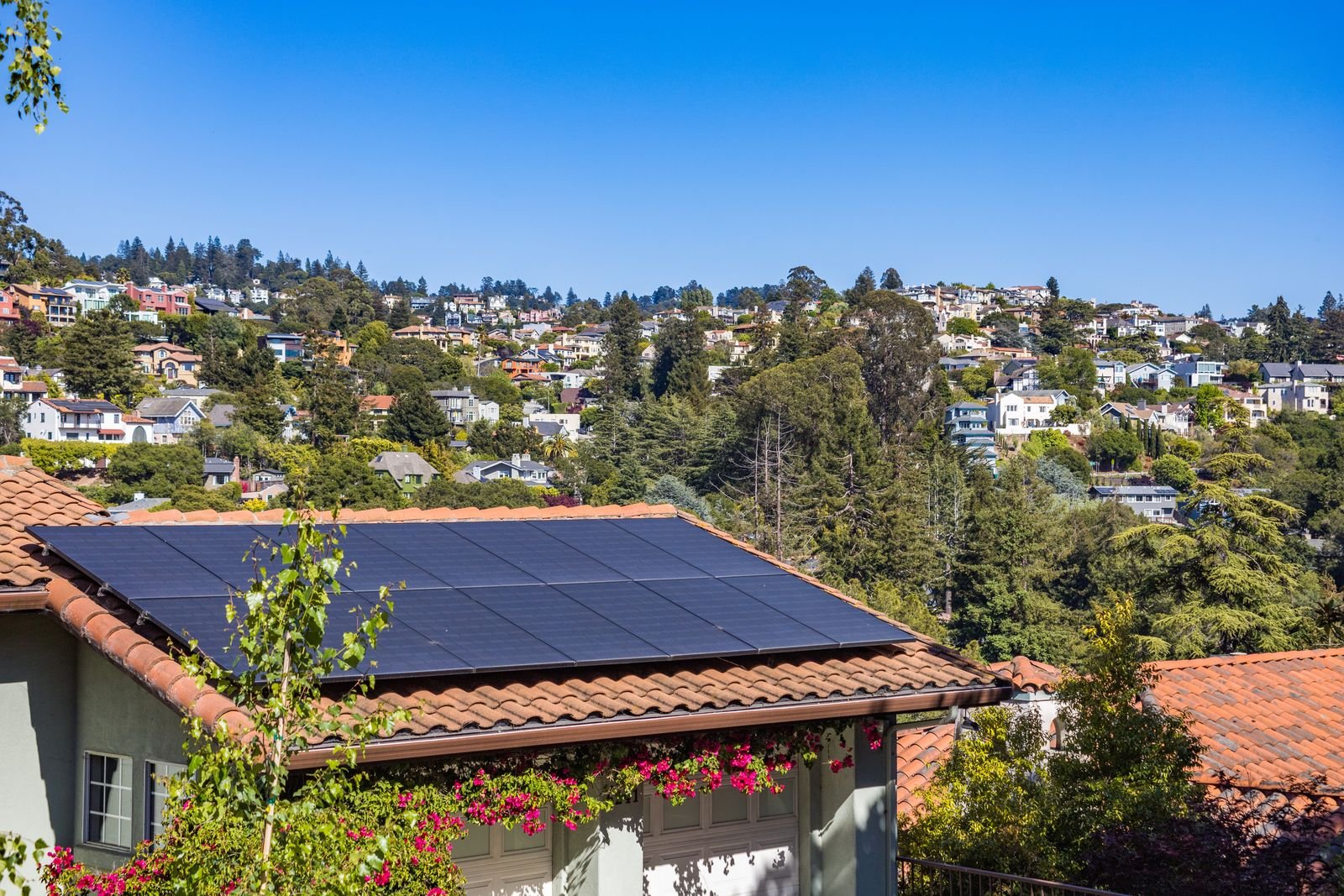 Suburban house with solar panels on the roof under a blue sky.
