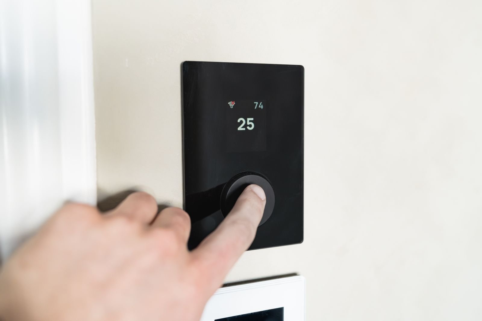 Hand adjusting a sleek smart thermostat on a wall.