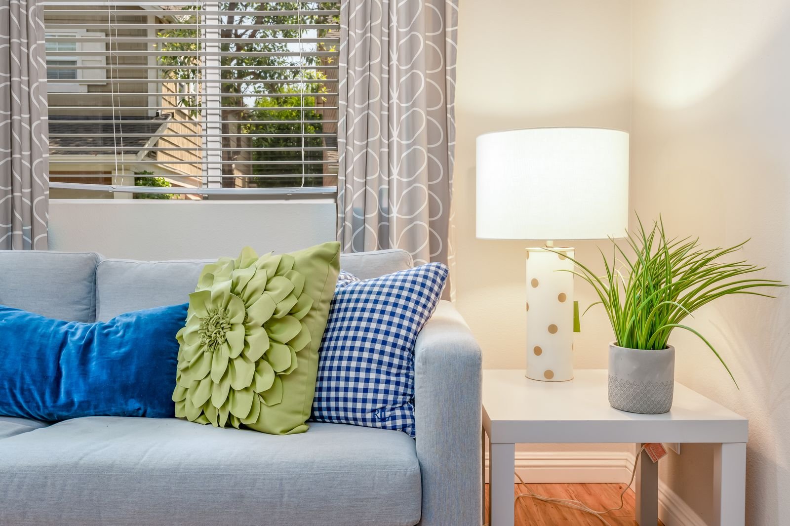 Sofa with colorful pillows, a table lamp and a green plant.