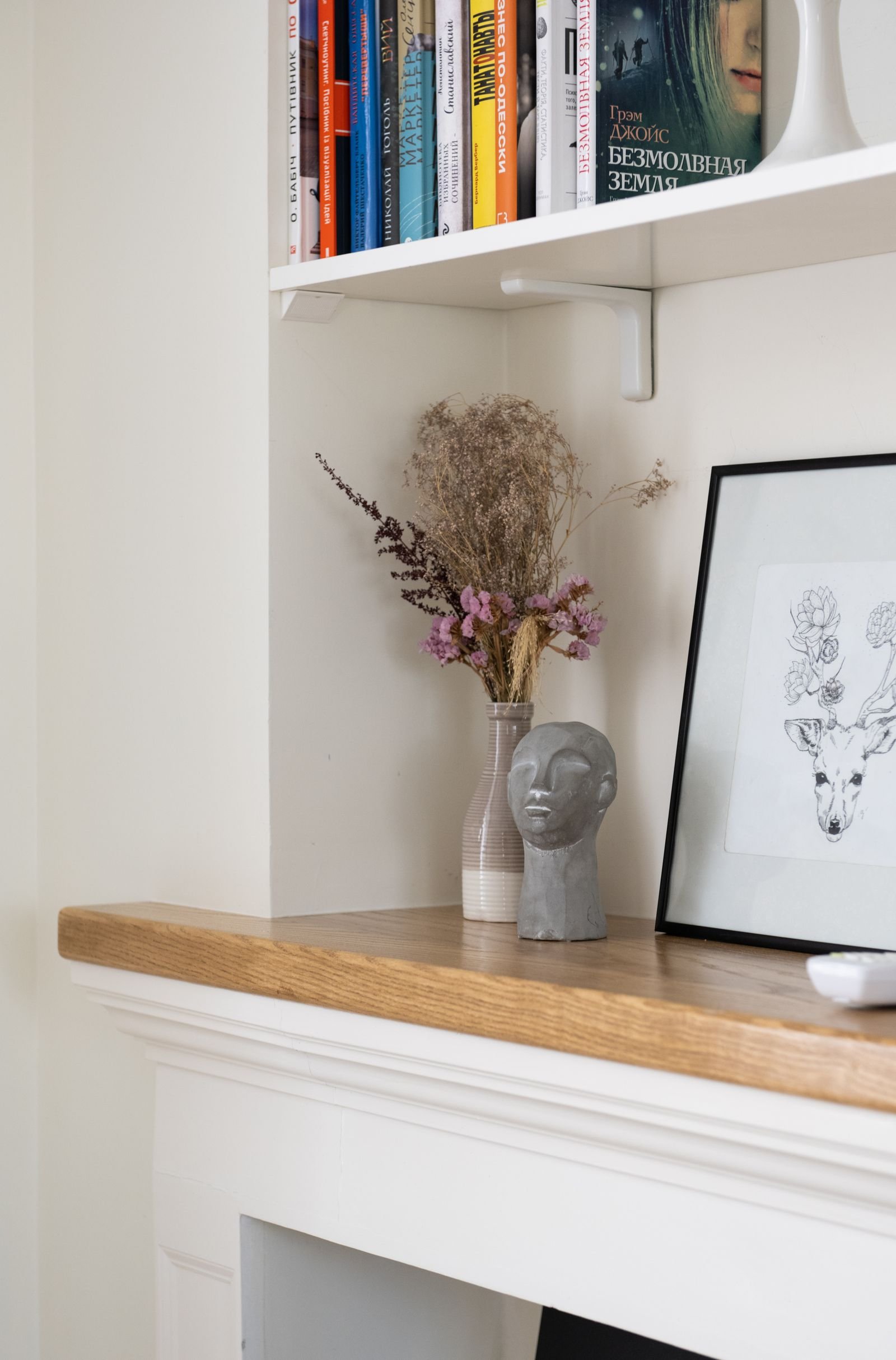 Shelves with books, a framed picture and a vase of dried flowers.