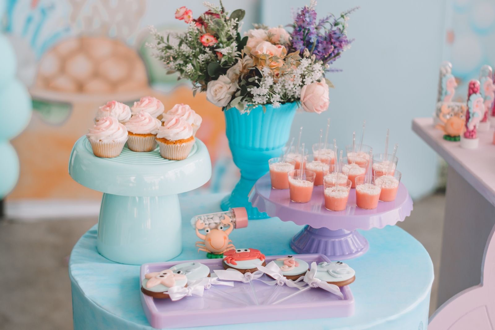 Dessert table with cupcakes, cookies and flowers in pastel colors.