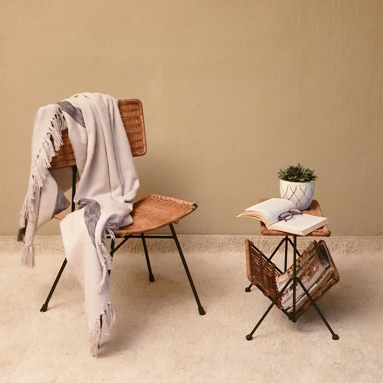 Reading nook with a wicker chair, a blanket, a small table and a plant.