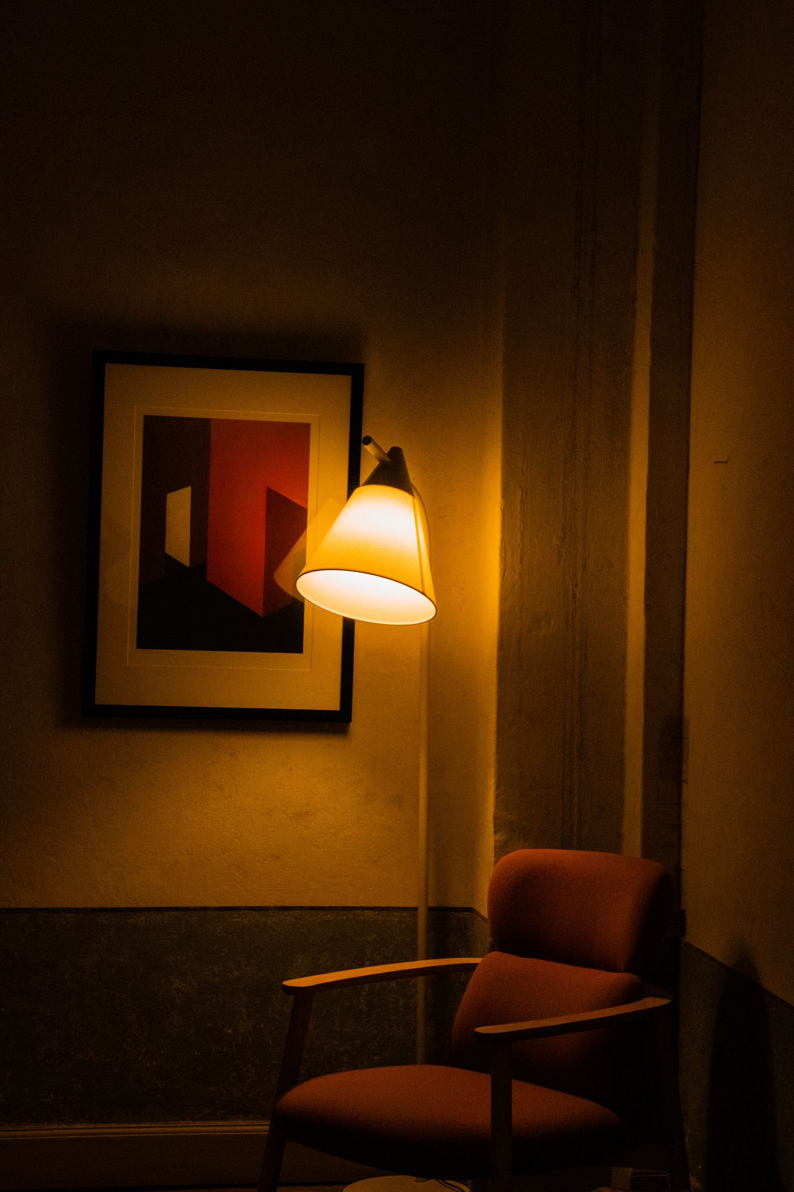 Armchair in a corner under warm lamp light beside abstract artwork.
