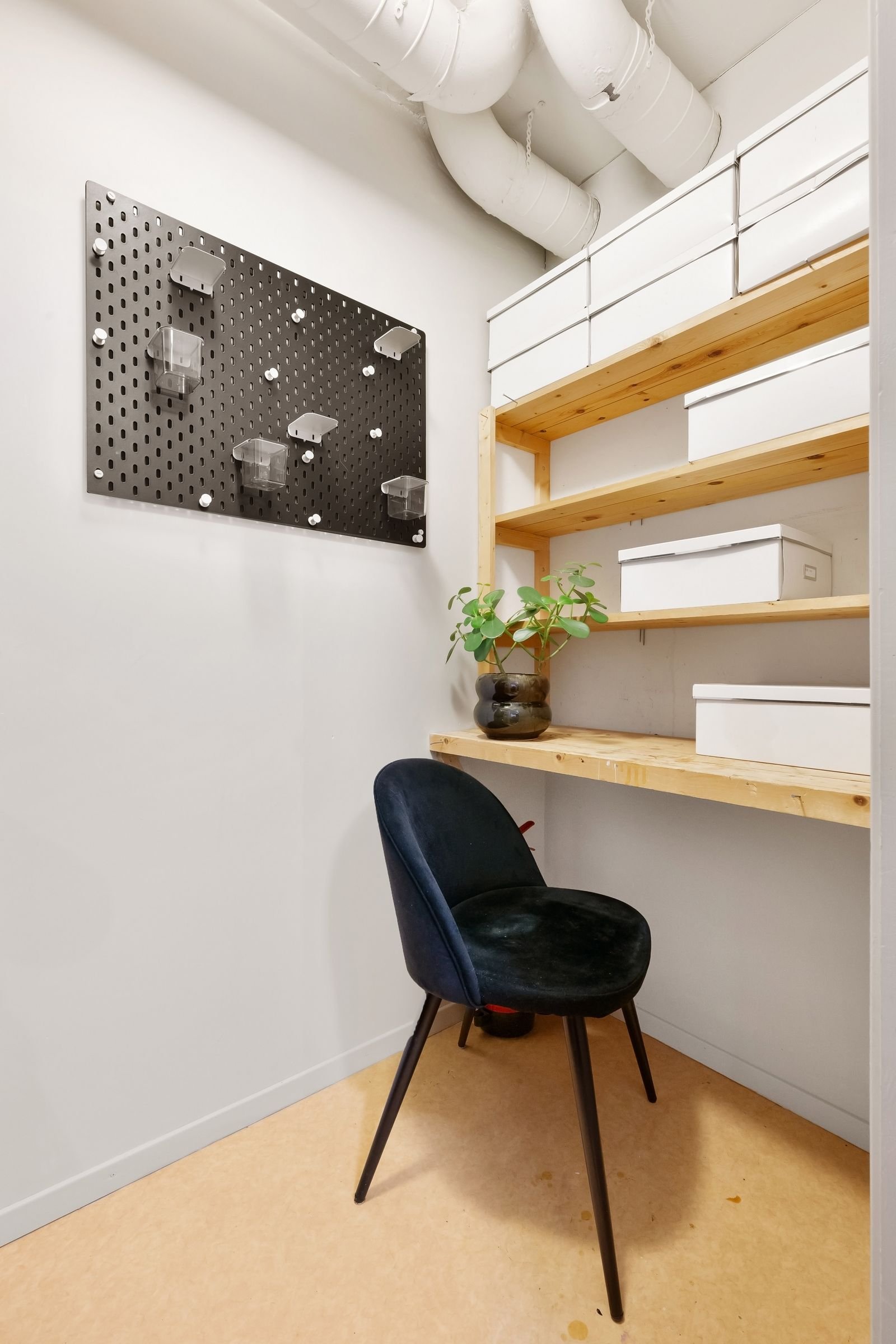 Minimalist home office corner with a black chair, wall shelves and a pegboard.