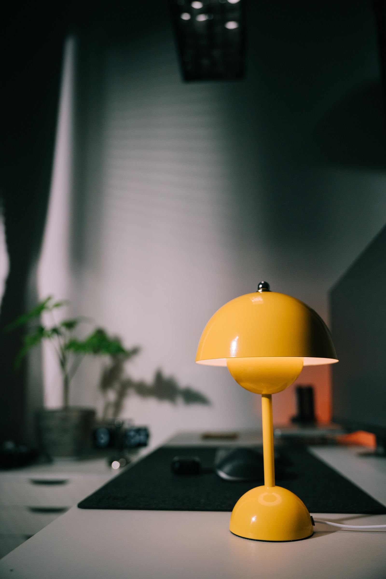 Yellow desk lamp lighting a minimalist workspace with a small plant.