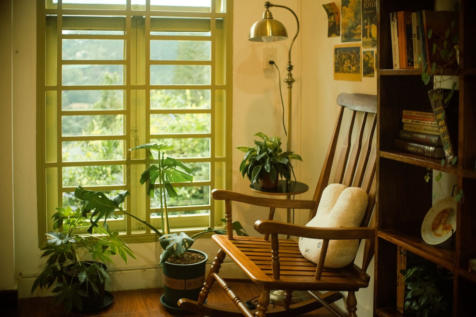 Wooden rocking chair with plants and books beside a window.