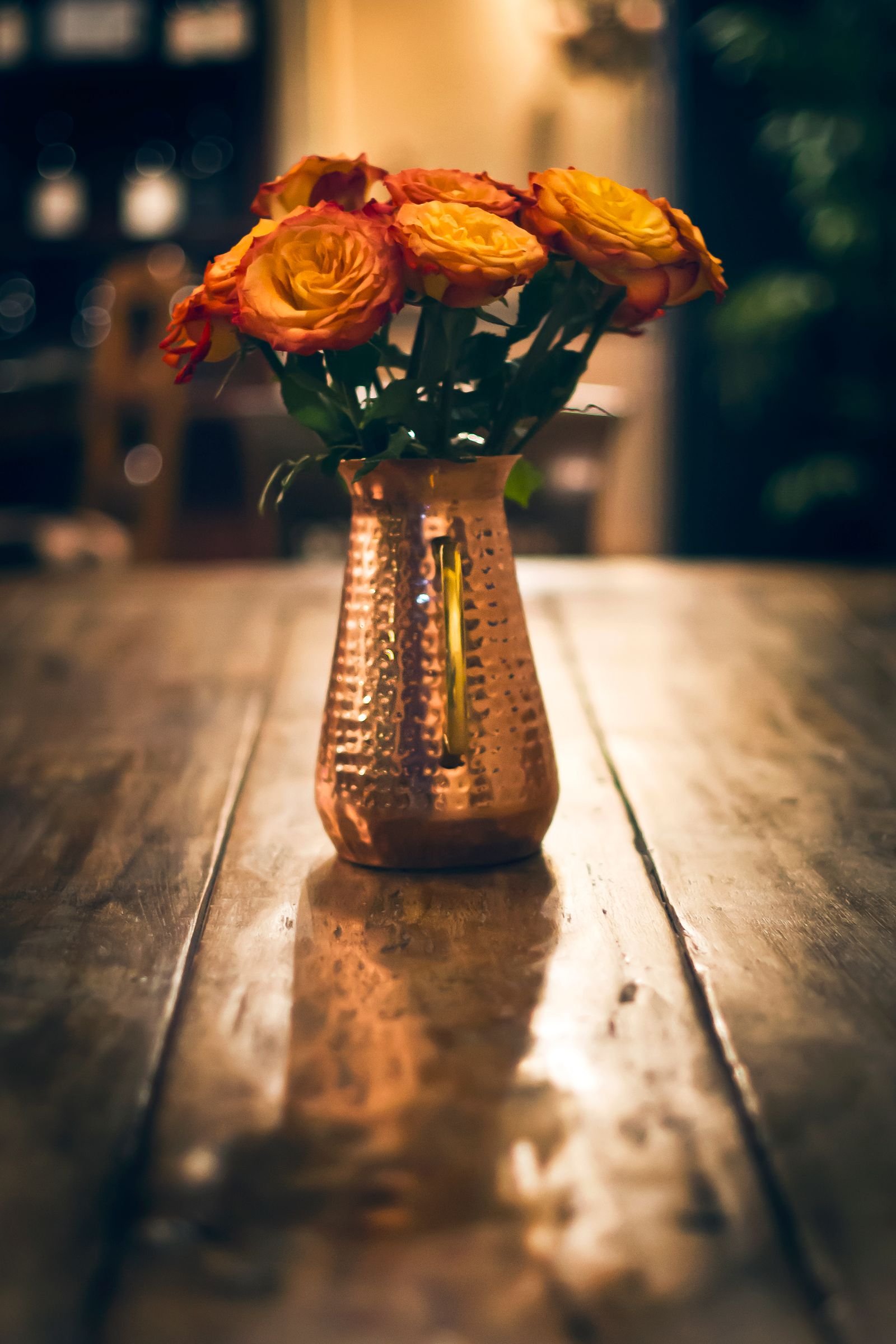 Colorful roses in a copper vase on a wooden table.