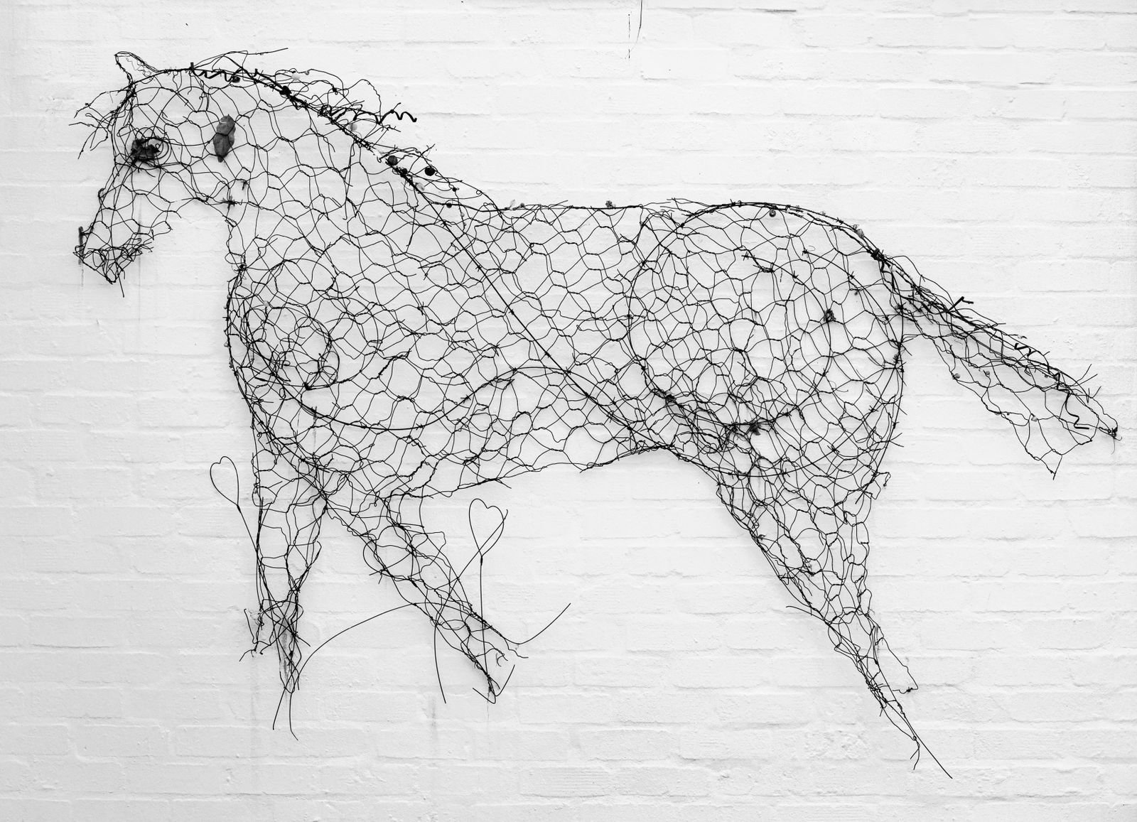 Wire horse sculpture mounted on a white brick wall.