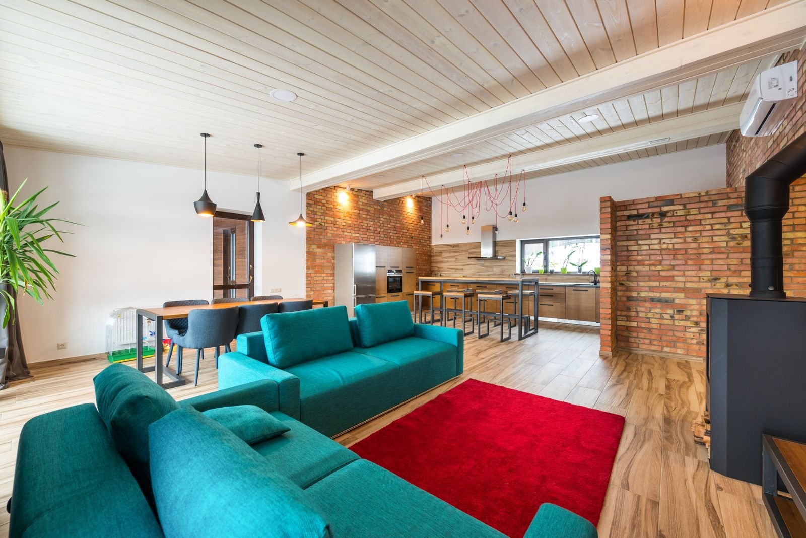 Living room with a brick wall, a teal sofa and a red rug on the floor.