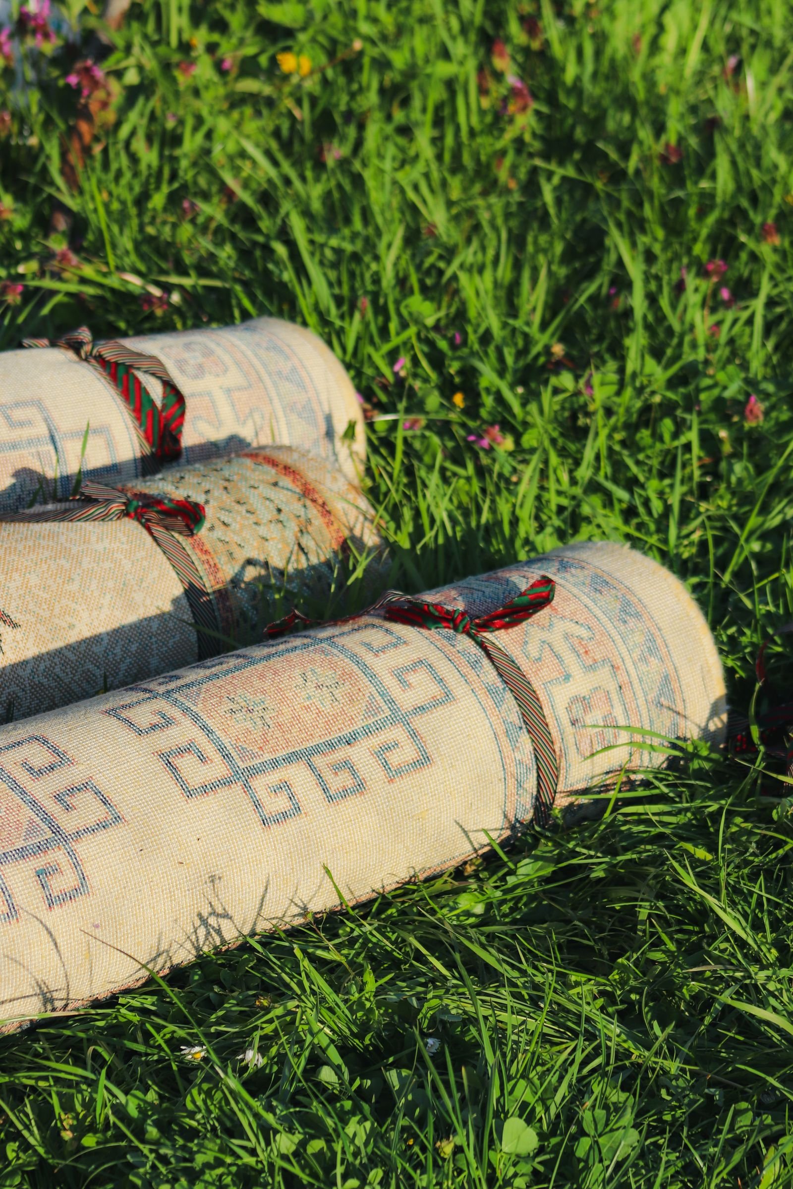 Patterned rugs laid out on green grass in the sunshine.