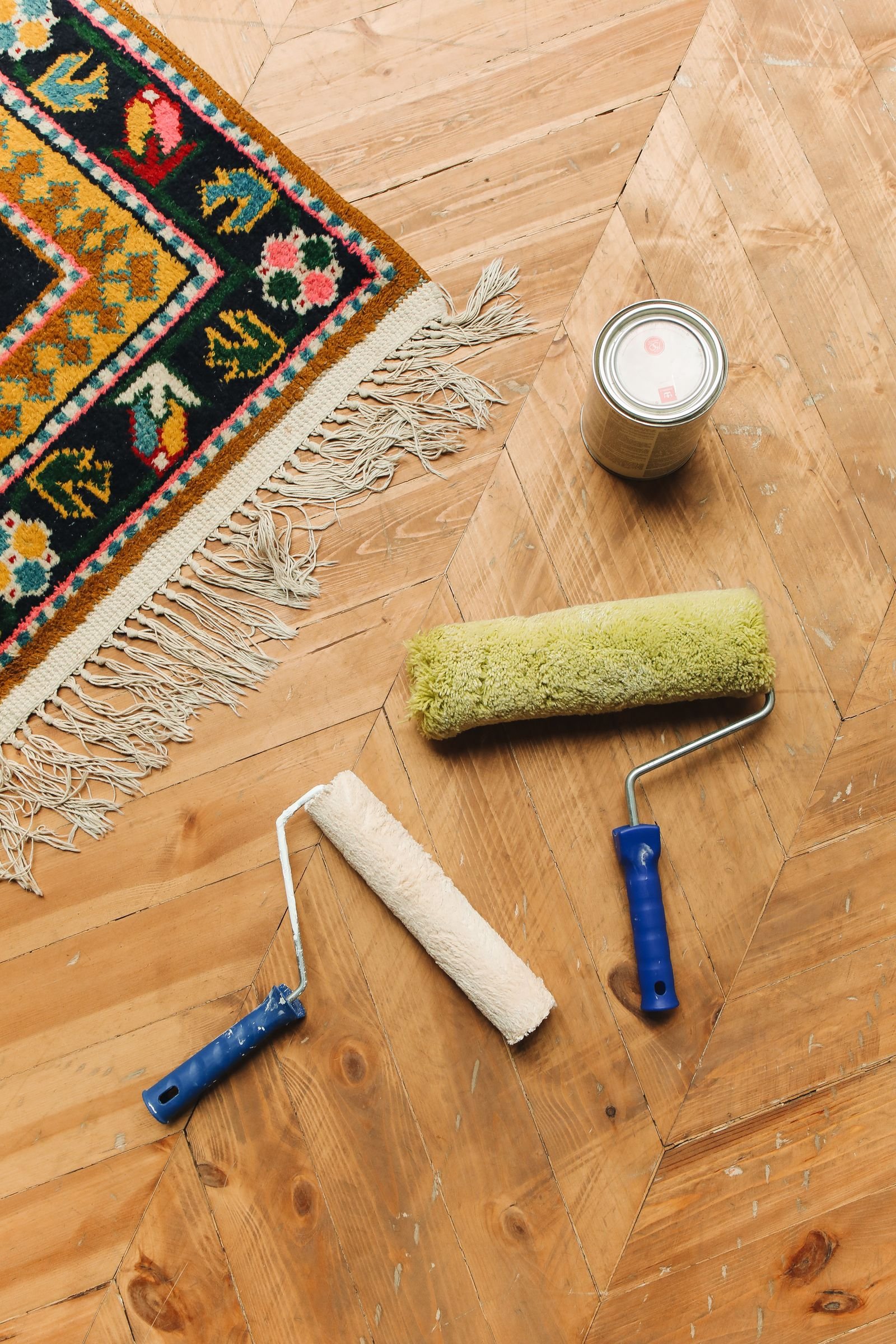 Decorative rug on a wooden floor beside paint rollers and a paint can.