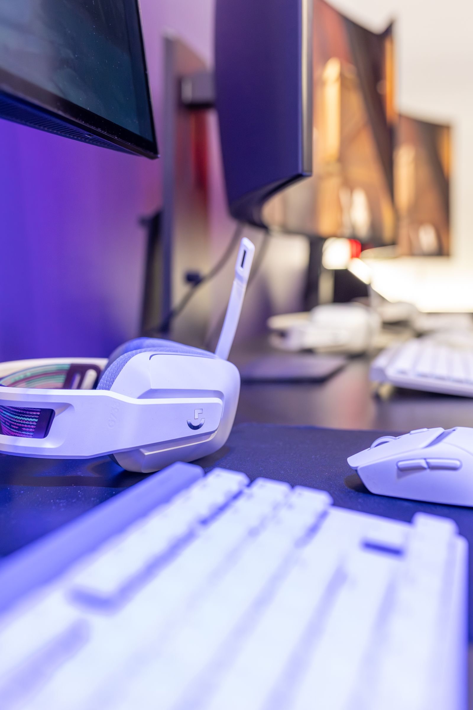 Gaming desk with a headset, keyboard and several monitors in purple light.